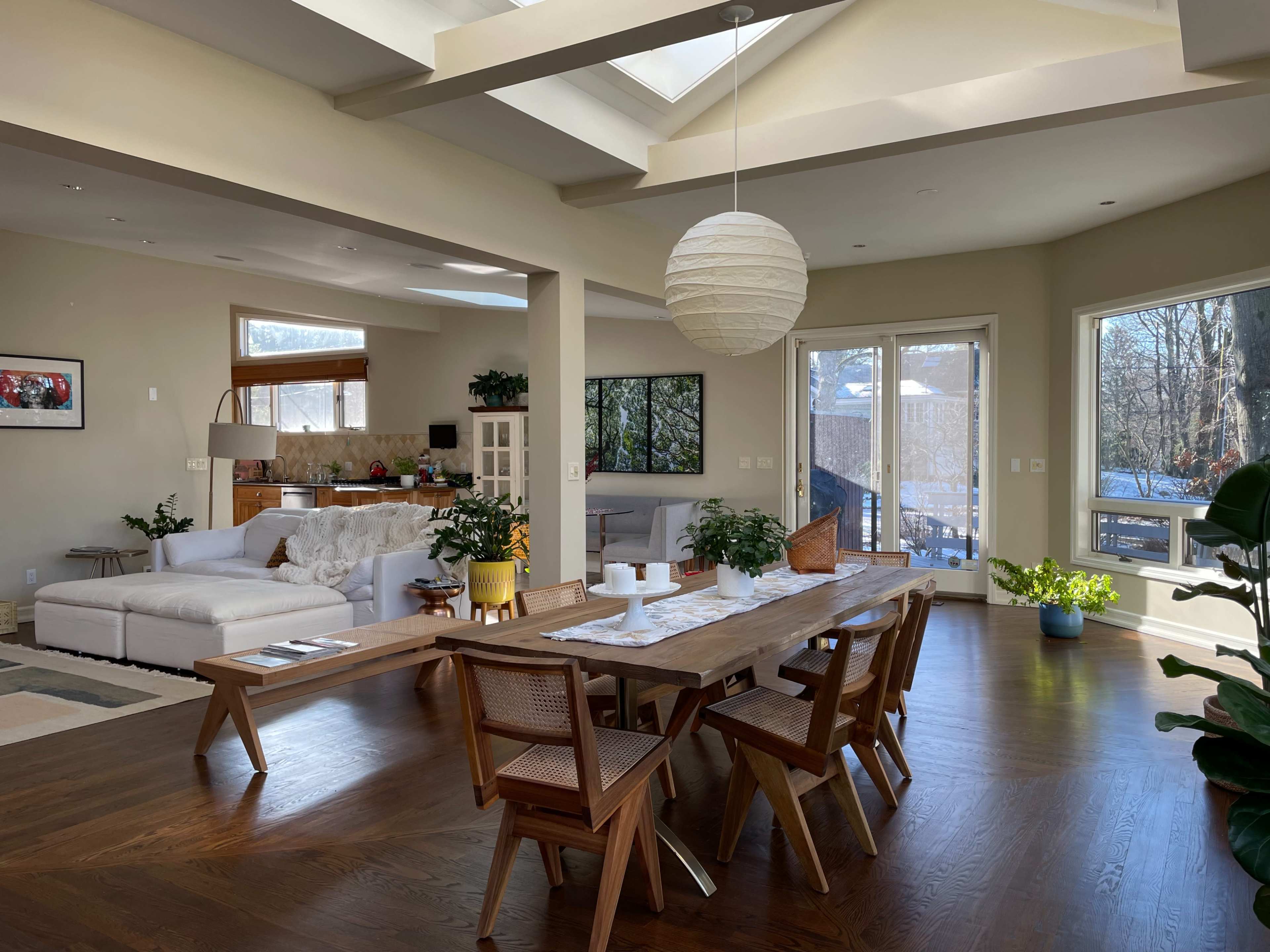 A spacious, open-concept living and dining area features a wooden dining table and a white couch, with large windows that provide ample natural light.
