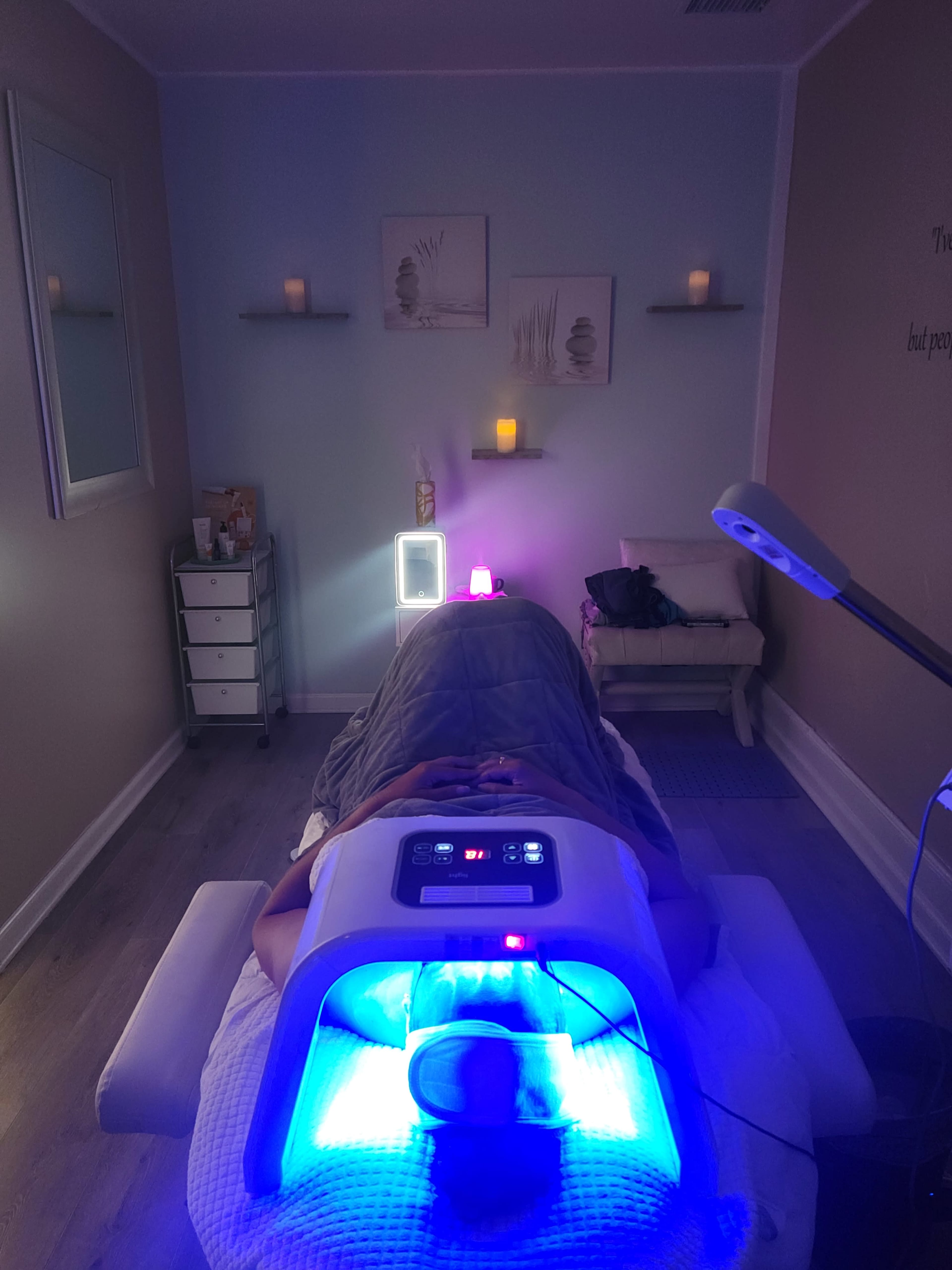 A person lies on a treatment table in a spa room, undergoing a light therapy session with blue LED lights while candles illuminate the space.
