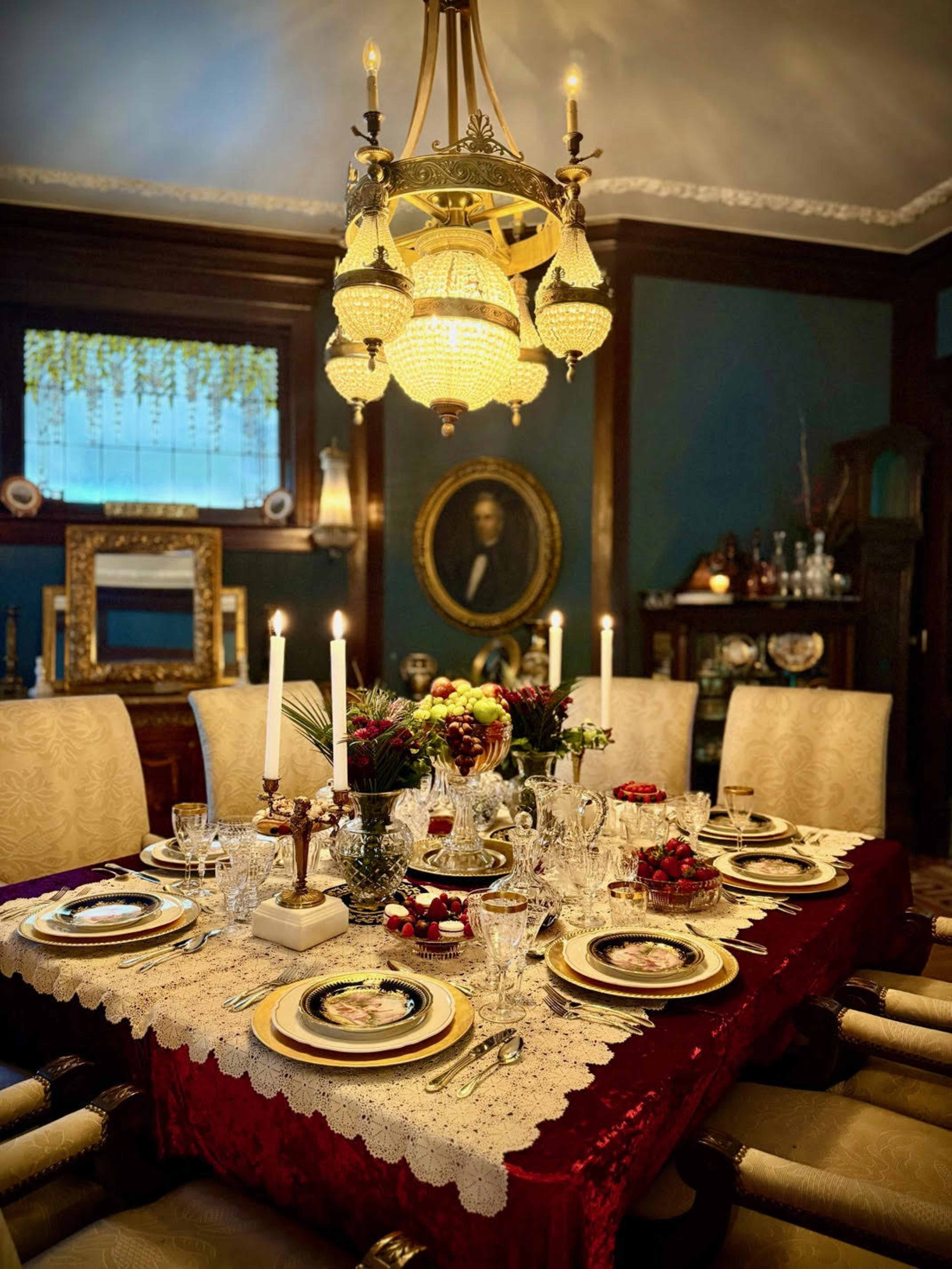 The image features an elegantly set dining table with fine china, crystal glasses, and candles, surrounded by plush chairs in a richly decorated room.