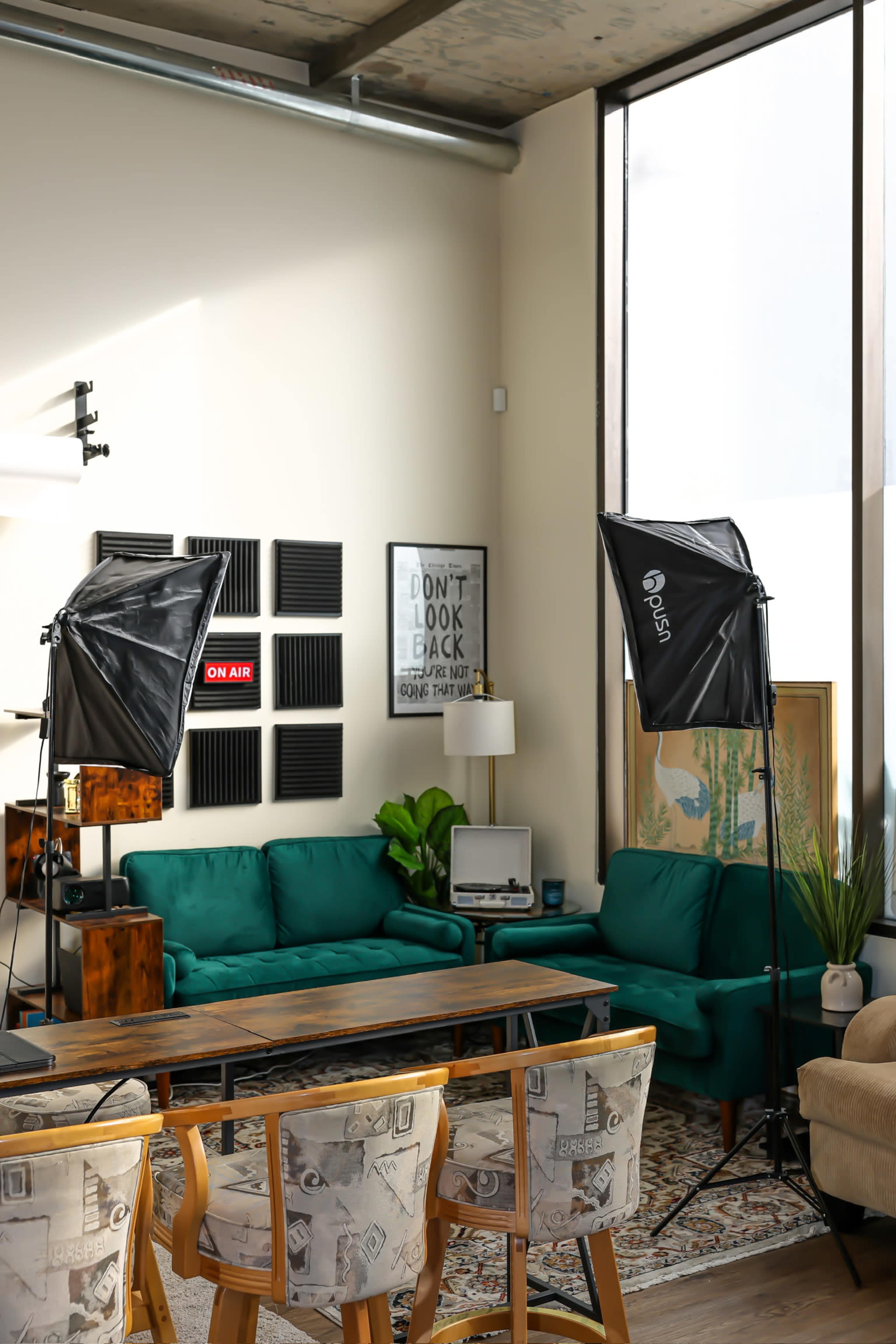 A well-lit modern living room features green sofas, a wooden table, and photography lights aimed towards the seating area.