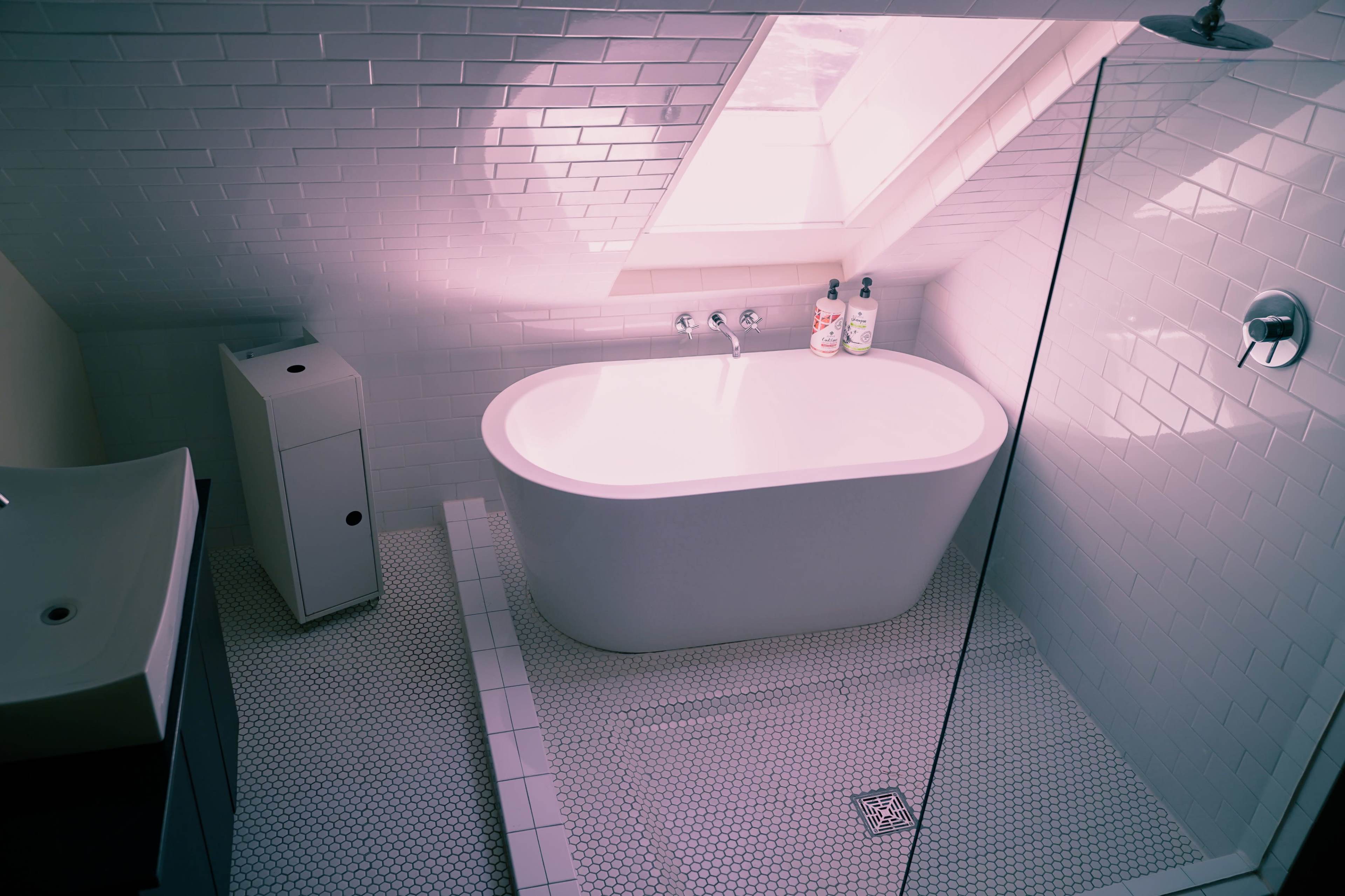 A modern bathroom featuring a freestanding white bathtub, a walk-in shower, and a skylight above.