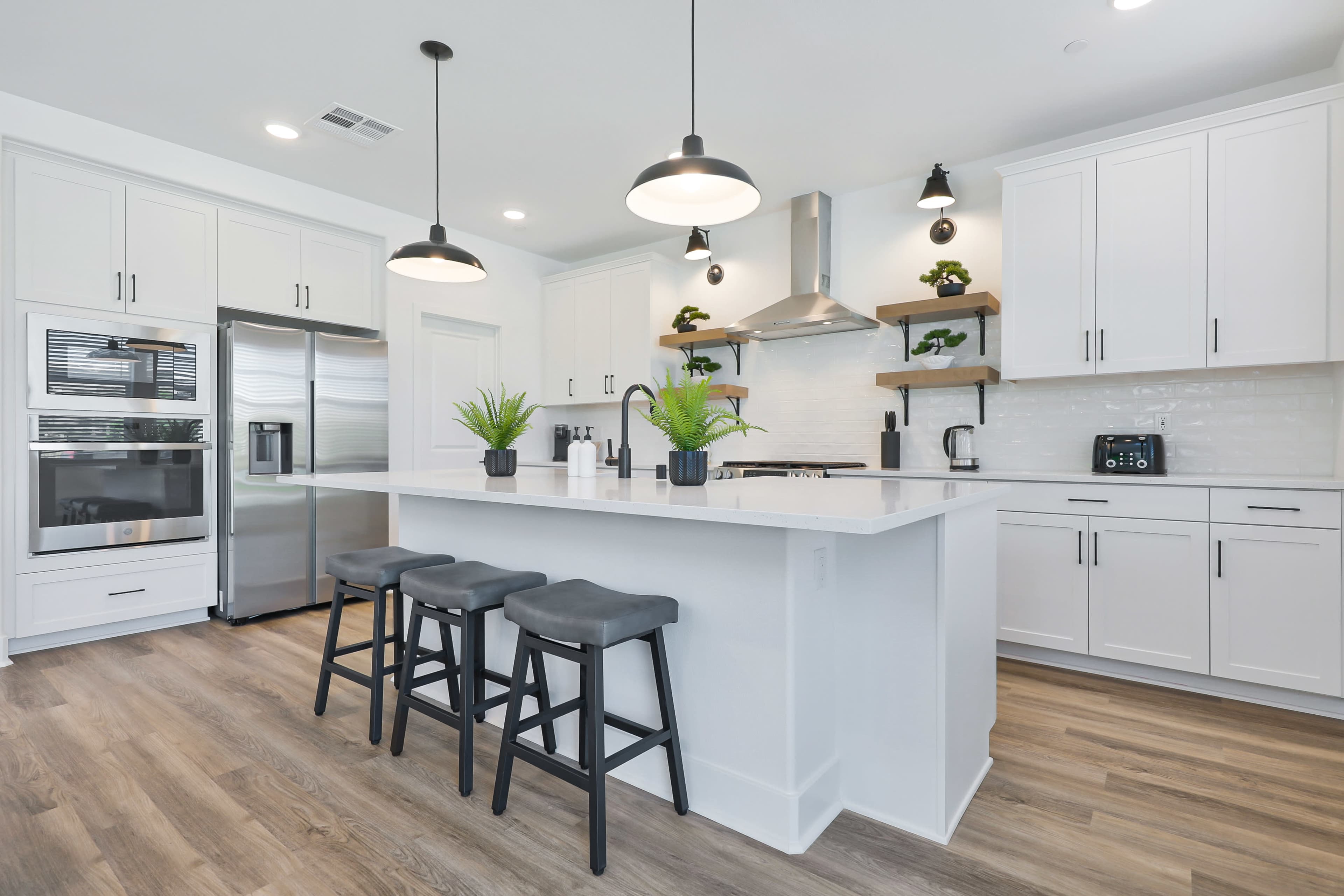 The image shows a modern kitchen featuring a central island with three stools, stainless steel appliances, and white cabinetry.