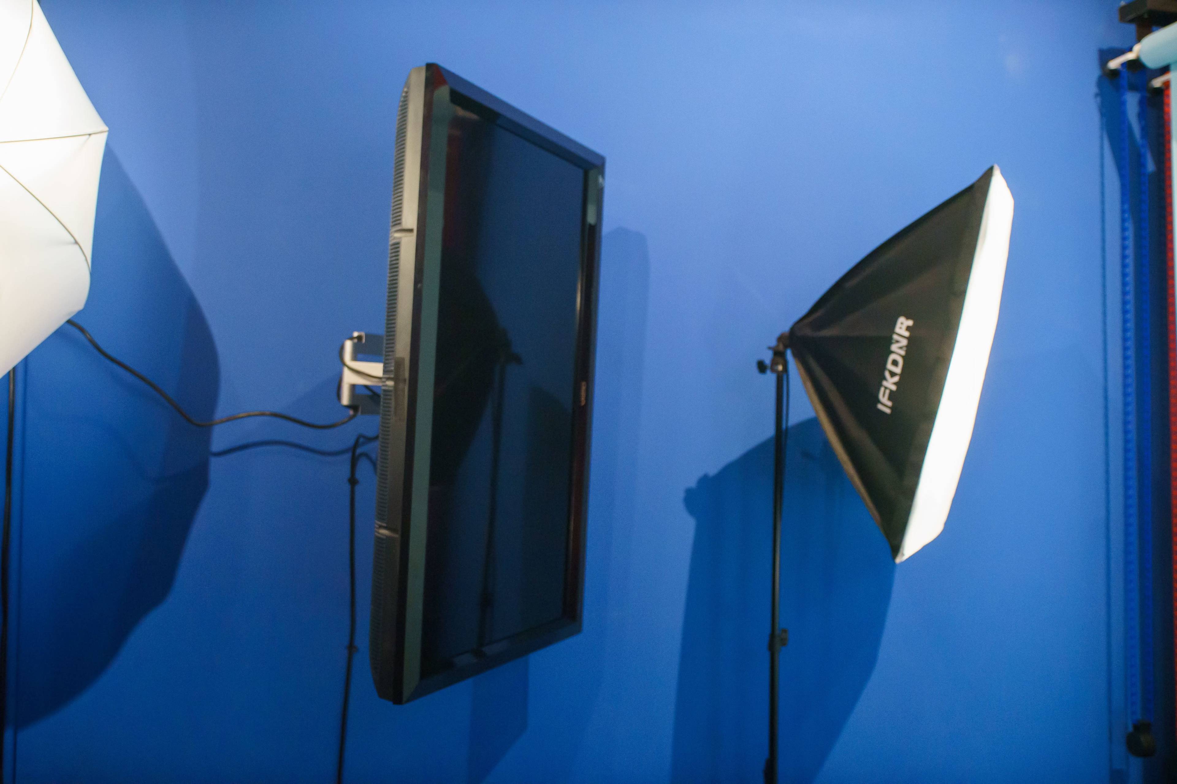 A wall-mounted television next to a photography lighting setup against a blue backdrop.