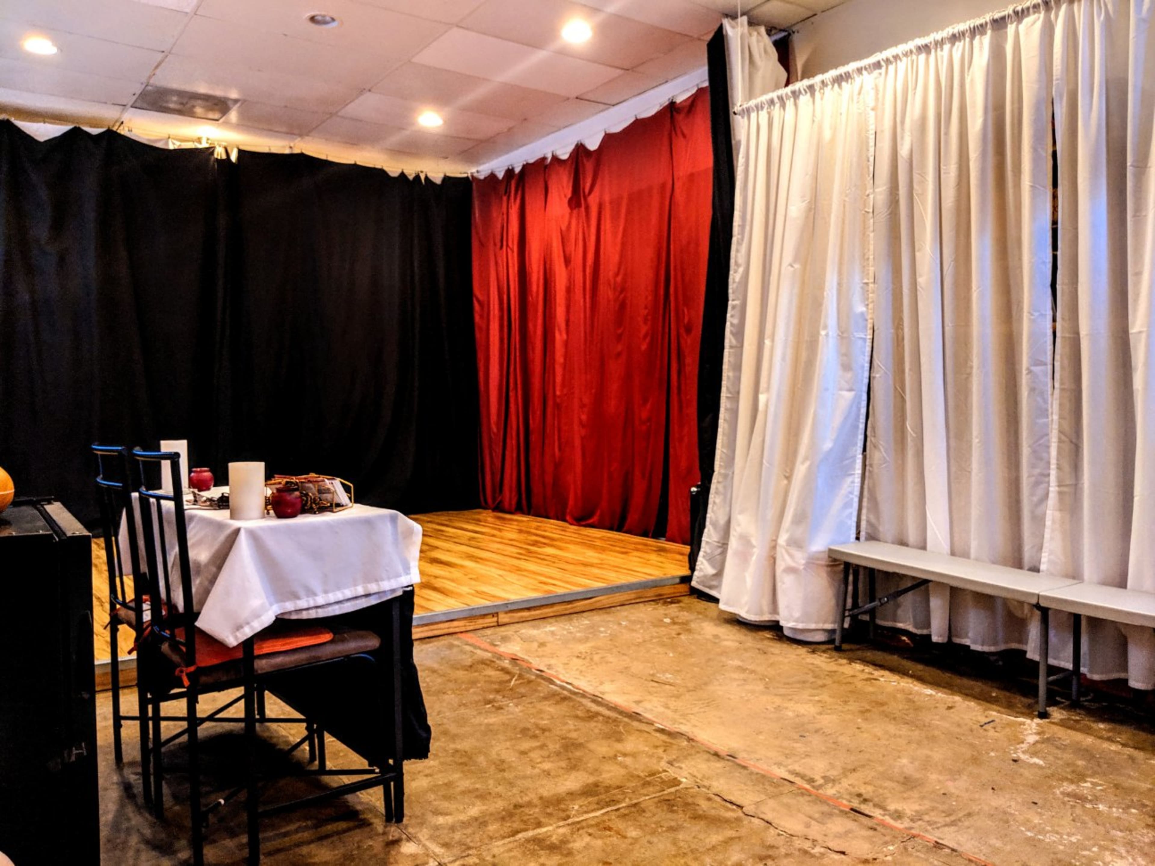 A partially set dining space with a table and chairs on one side and a performance stage draped in black and red curtains on the other.