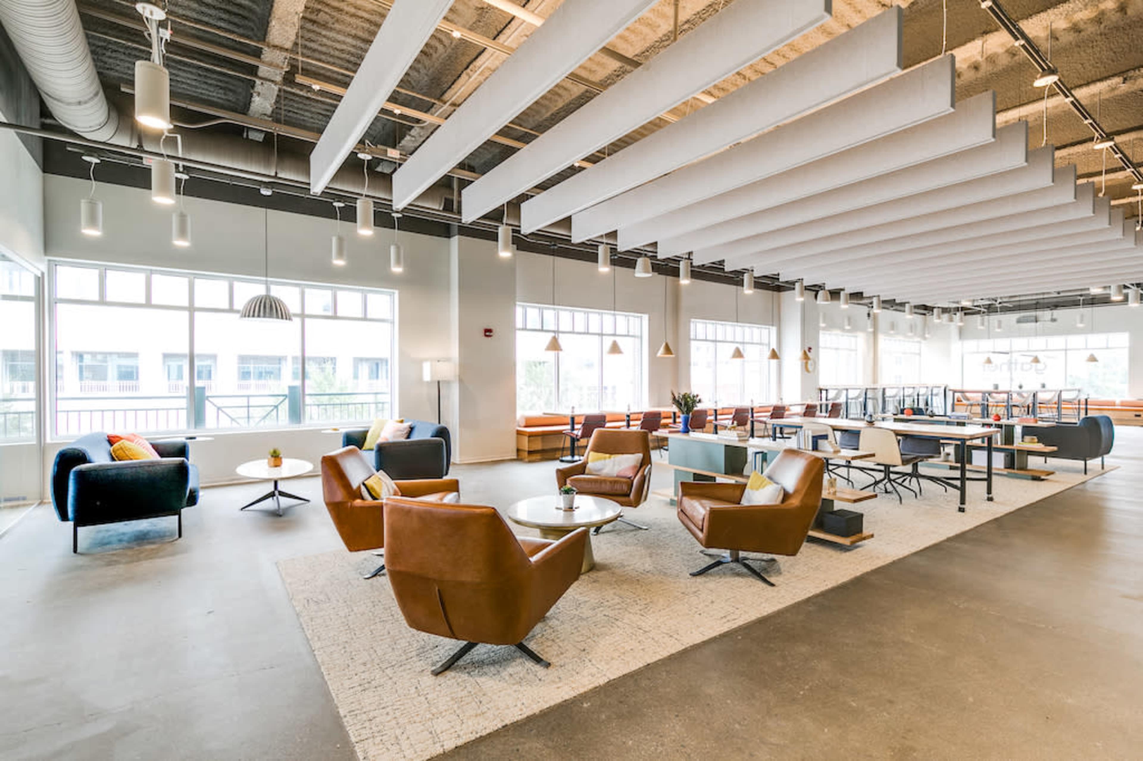 A modern, spacious lounge area with various seating options, including brown leather chairs and light-colored sofas, arranged around coffee tables on a gray floor.