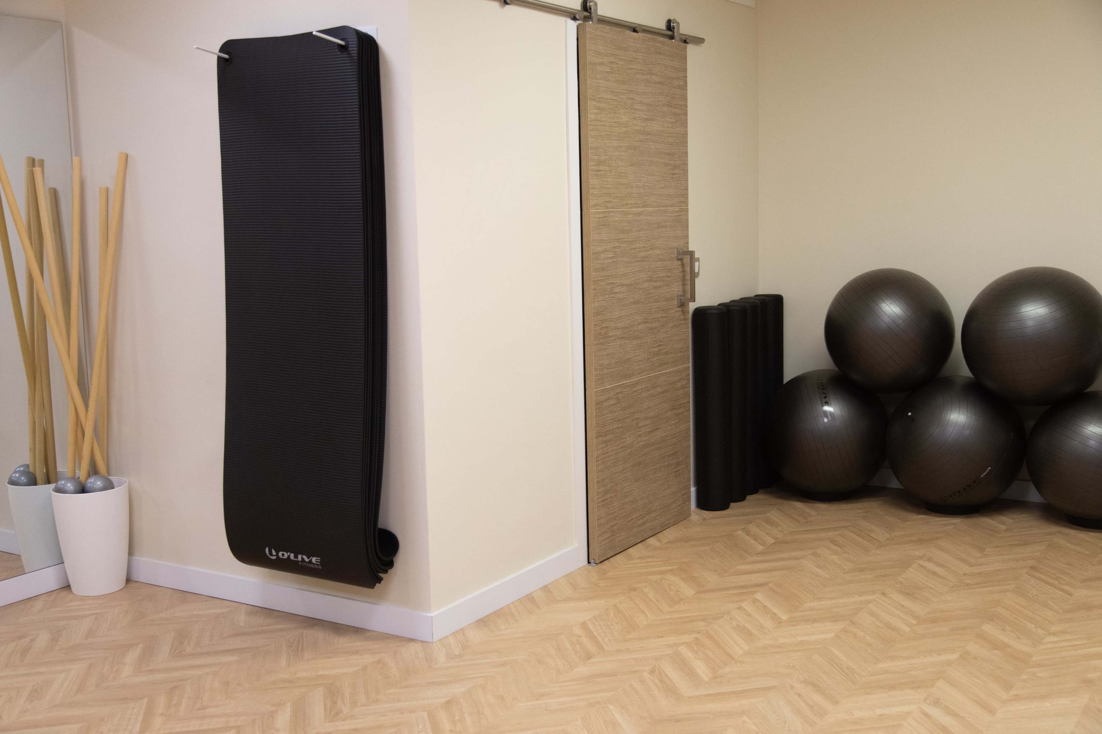 A fitness room featuring a rolled yoga mat hanging on the wall, exercise balls stacked in the corner, and a mirrored wall with wooden poles in a container.