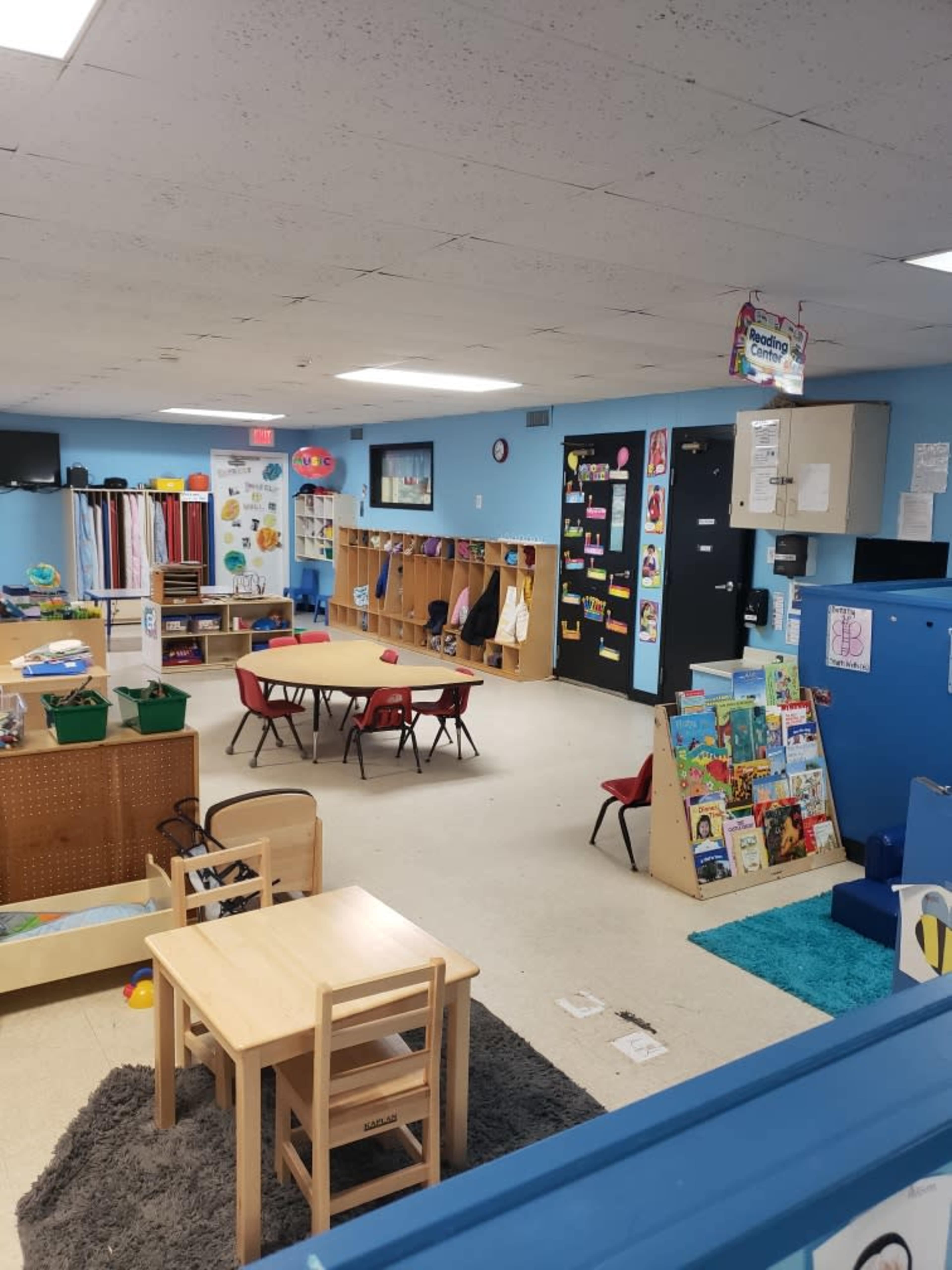 A classroom is arranged with tables and chairs, storage units, and educational materials displayed on the walls.