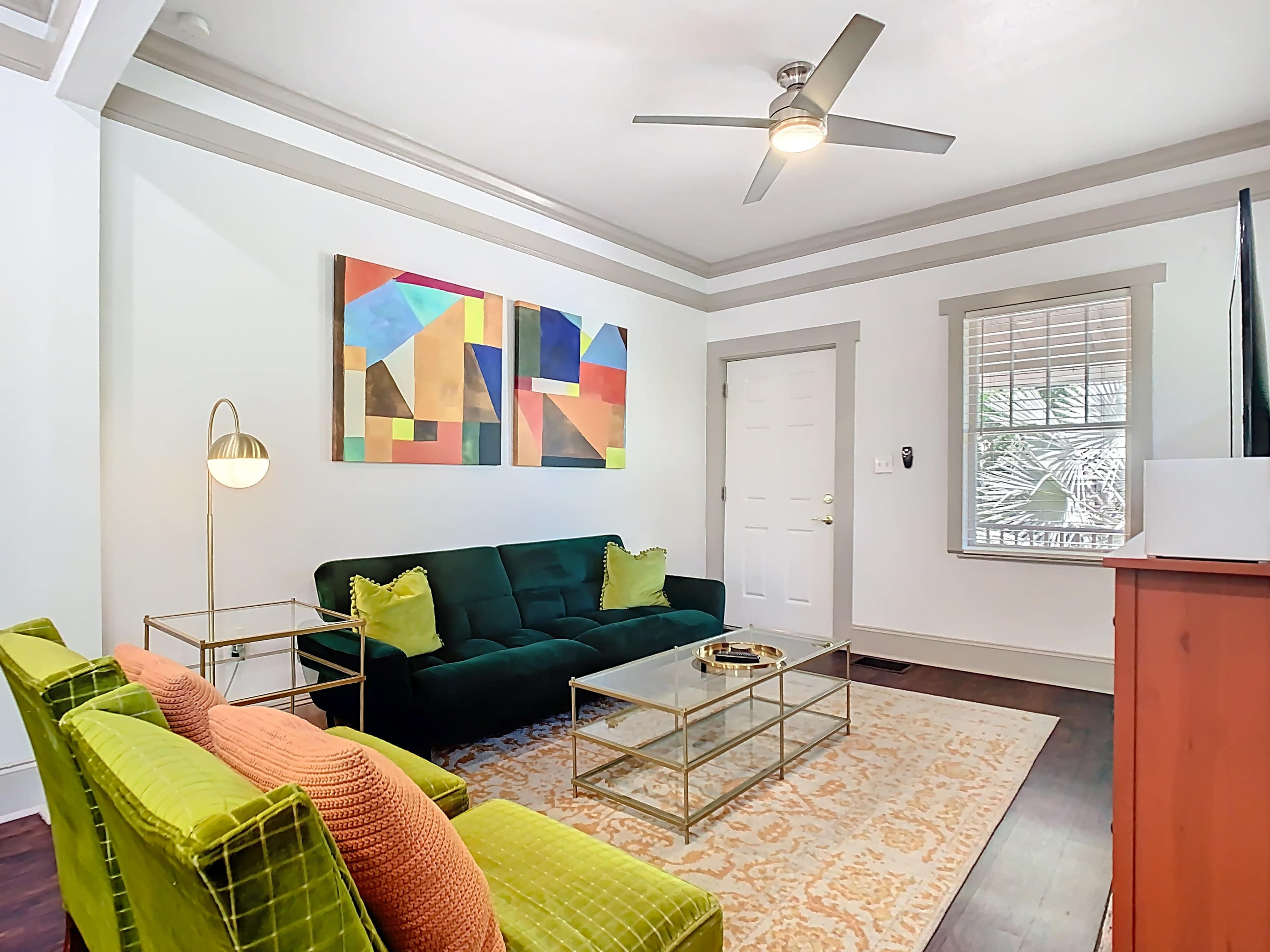 The image depicts a modern living room featuring a green couch, two lime green armchairs, a glass coffee table, and abstract wall art, with natural light coming through a window.