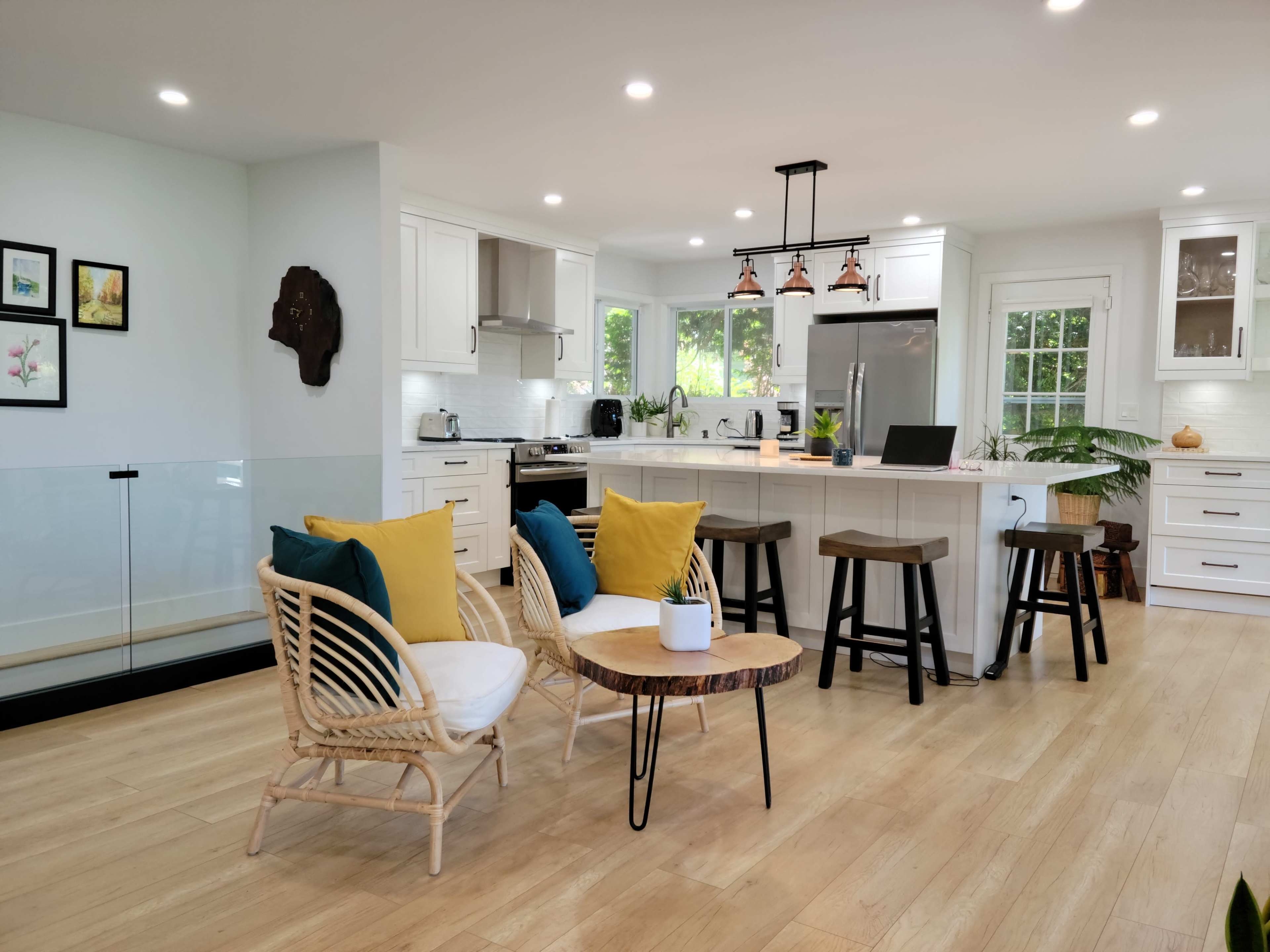 A modern kitchen with white cabinetry, a central island, and a seating area featuring rattan chairs and a small table.