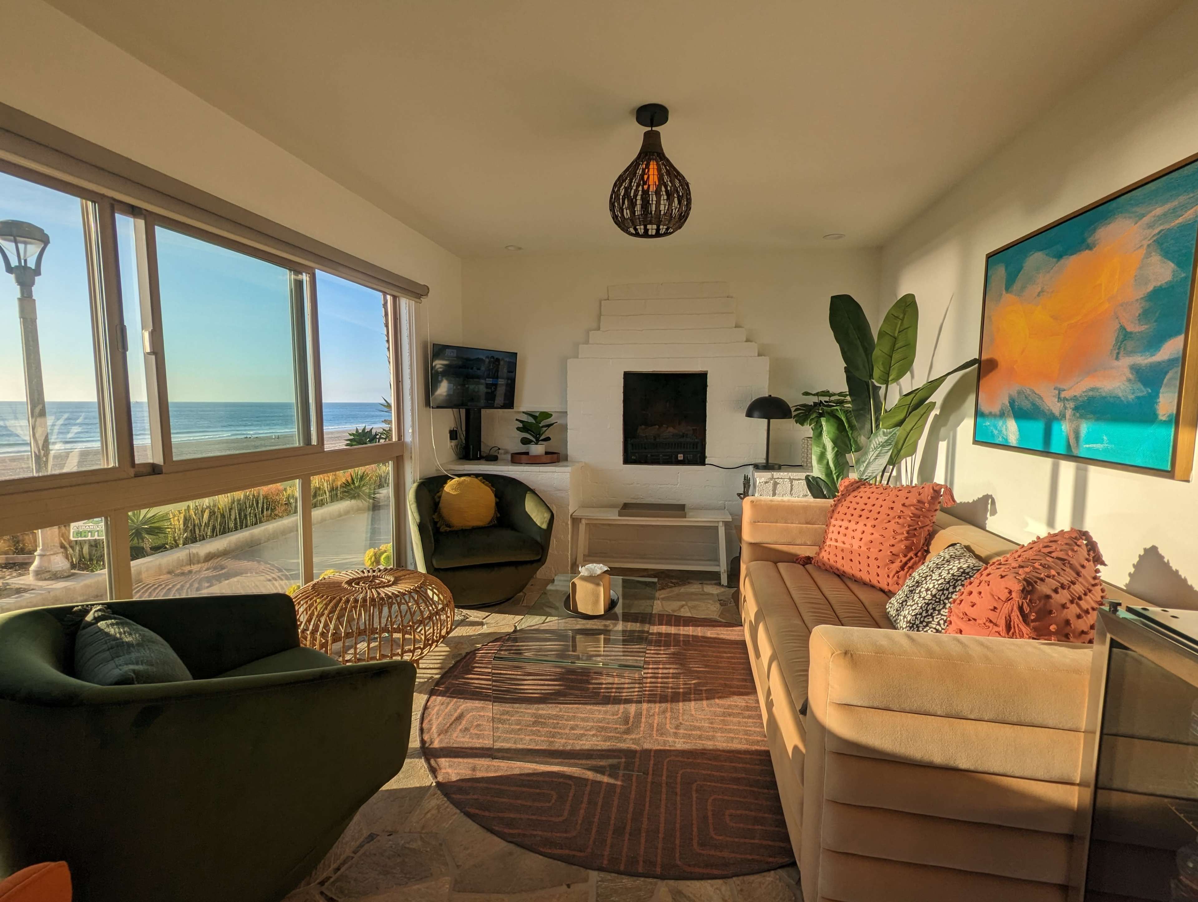 A modern living room with a view of the ocean, featuring a sofa, two green chairs, a coffee table, and a large window letting in natural light.