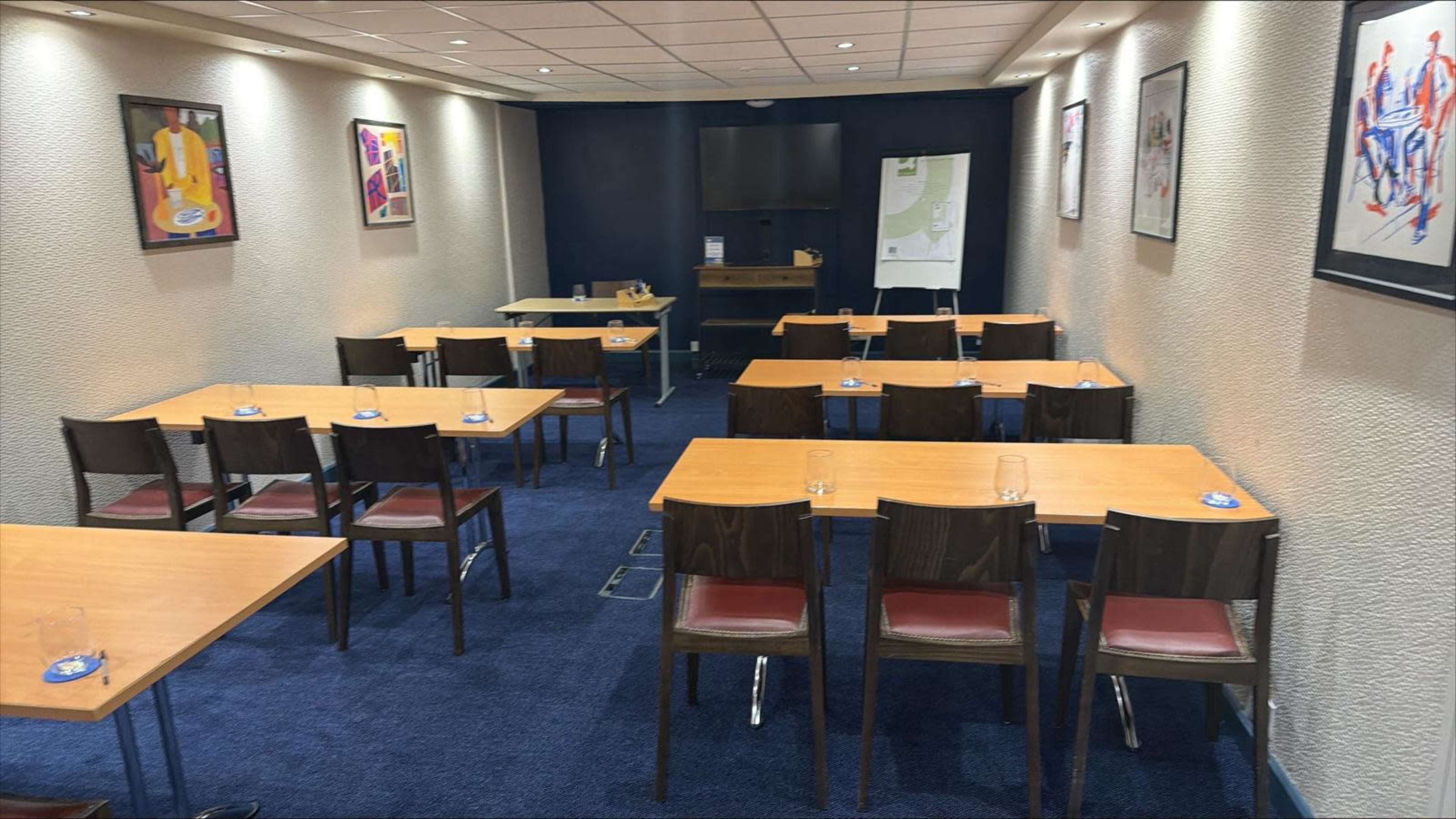 A conference room is set up with several tables and chairs, featuring a television and a presentation board at the front.