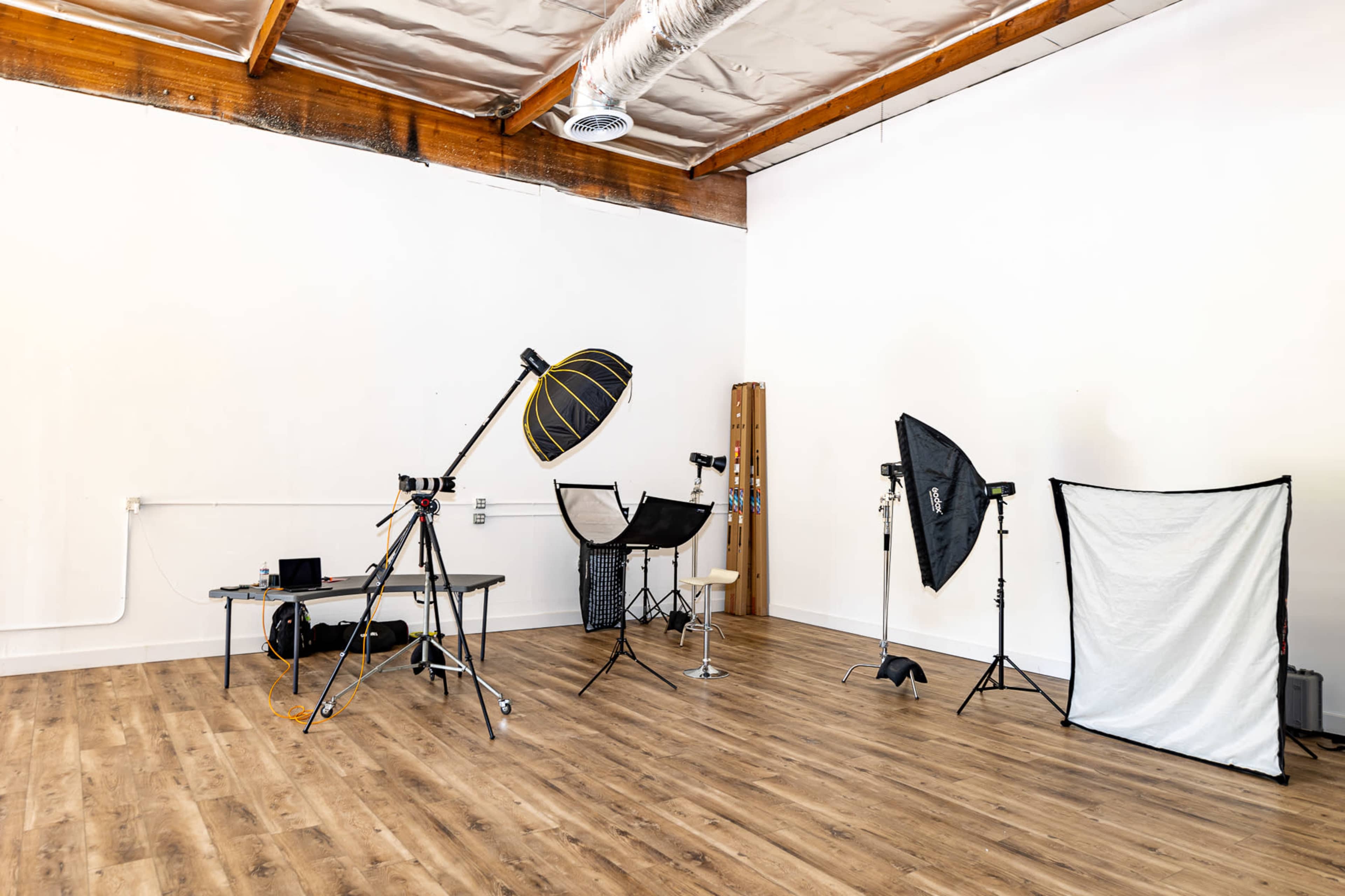 A photography studio with various lighting equipment, a table, and backdrops set against a plain wall and wooden floor.