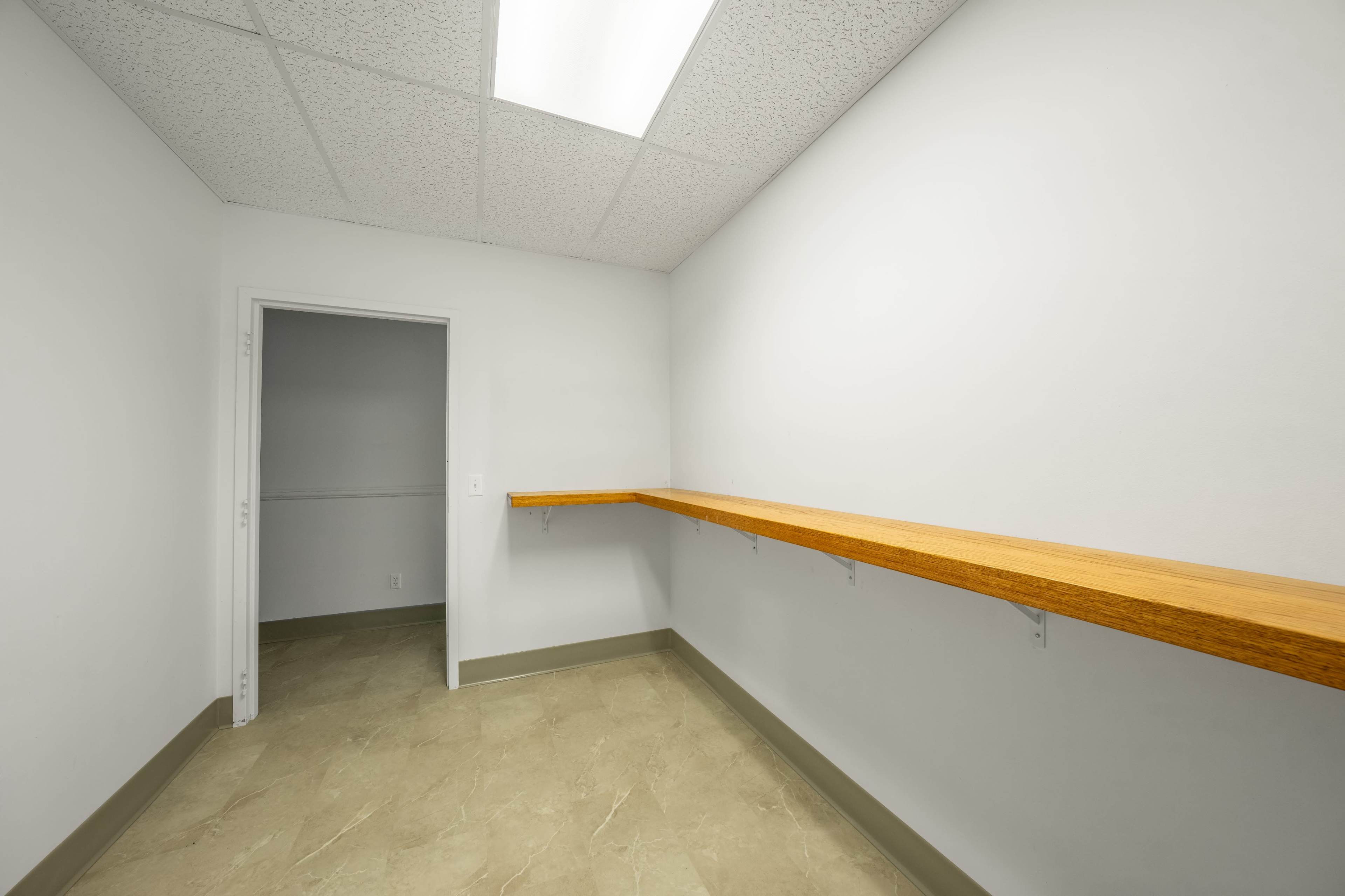The image shows a small, empty room with a wooden ledge against one wall and a doorway leading to another space.