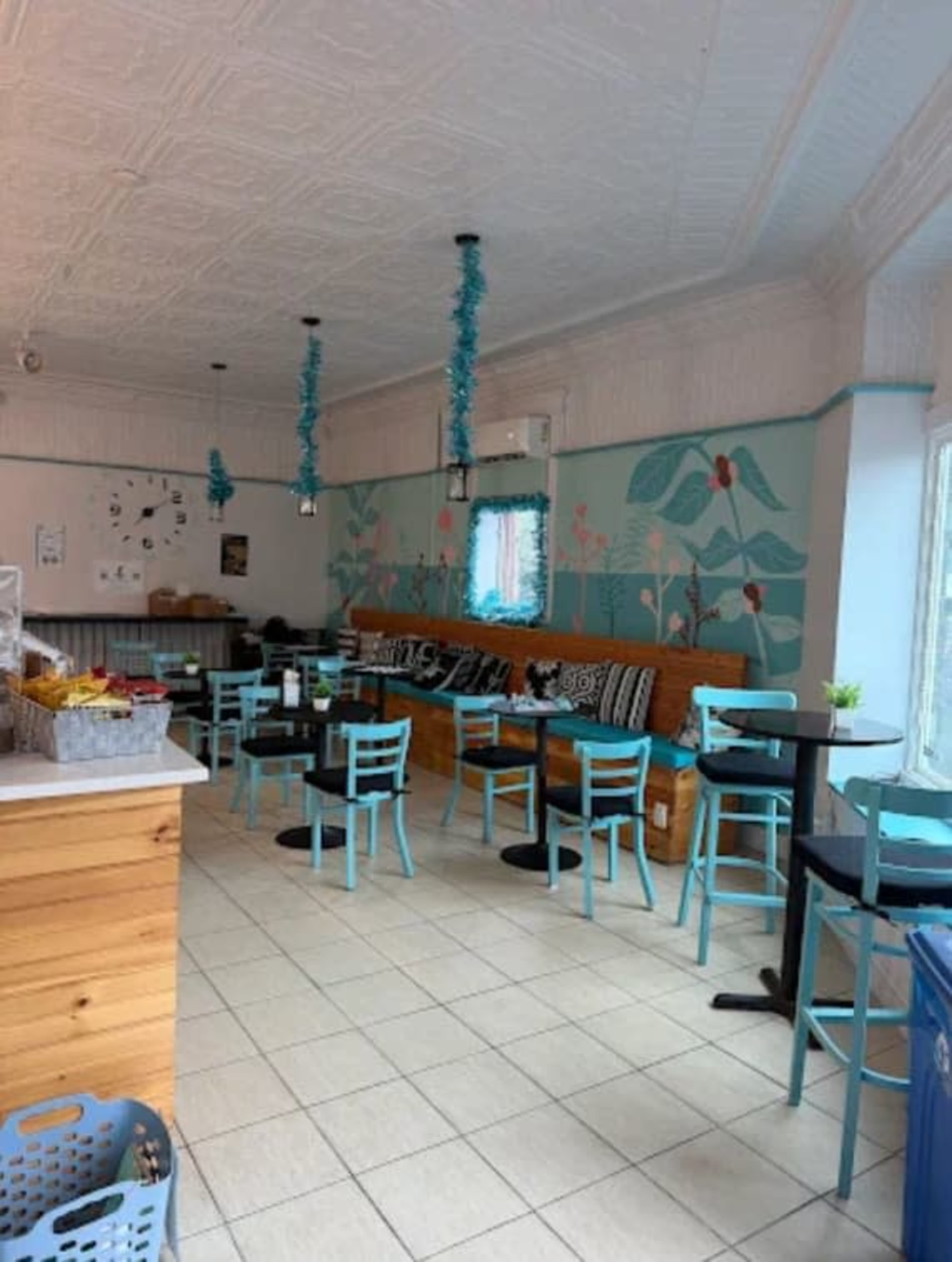 The image depicts a cozy café interior featuring turquoise chairs, a wooden bench, and floral mural decor on the walls.