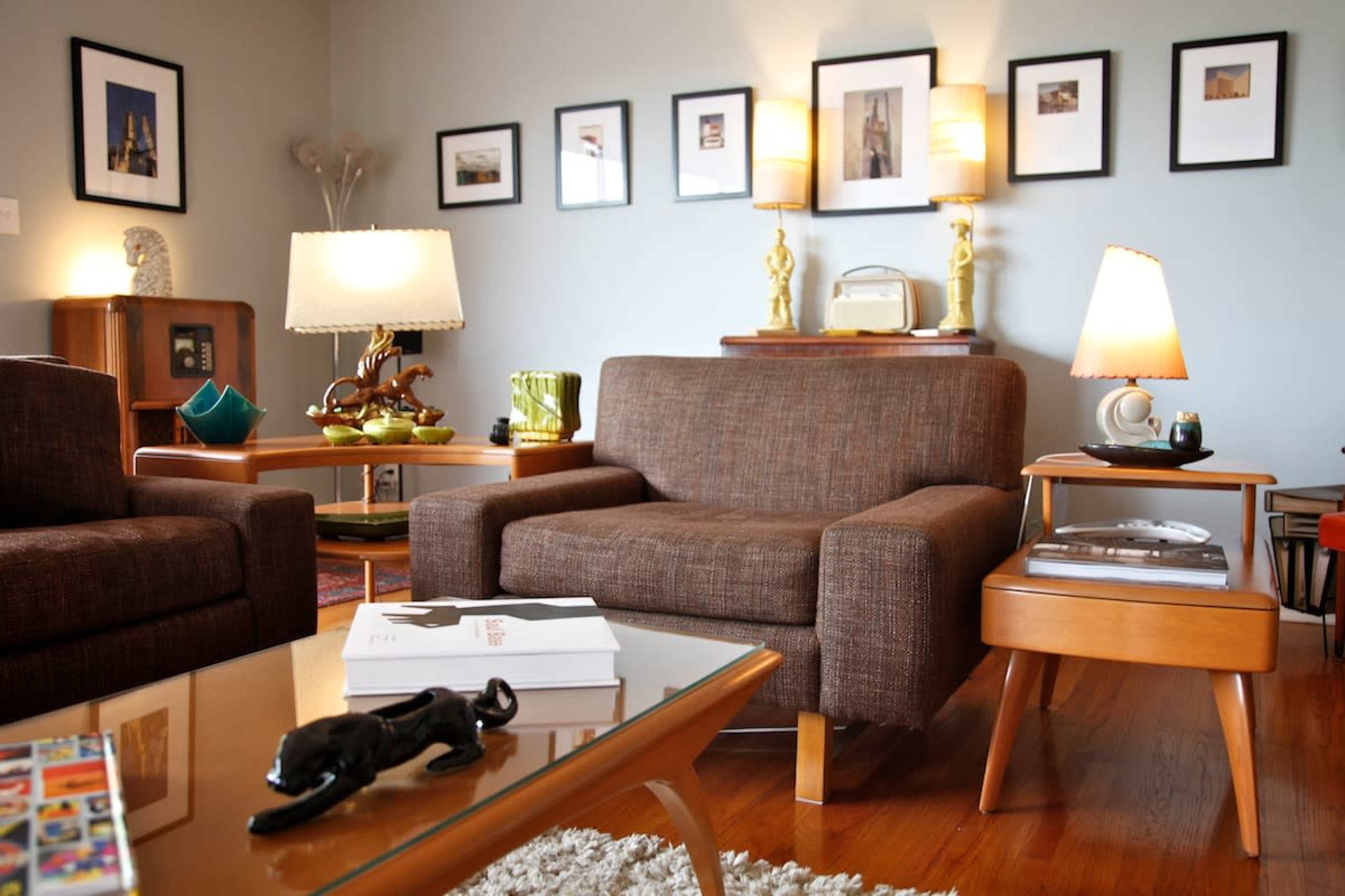 The image shows a cozy living room with two brown sofas, a glass coffee table, and framed pictures on the walls.