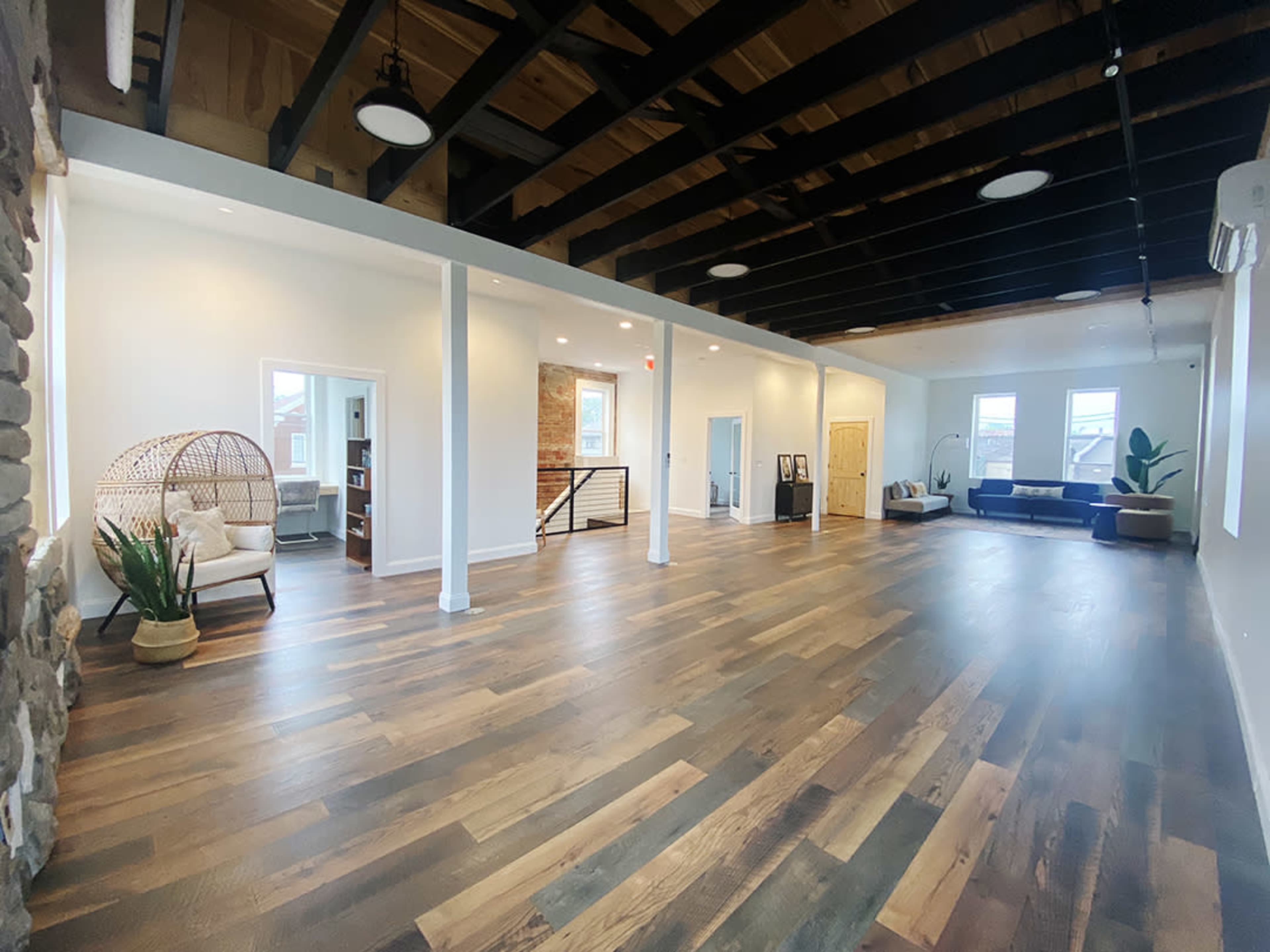 An open, spacious interior with hardwood flooring, exposed beams, and a mix of seating areas, including a wicker chair and a sofa.