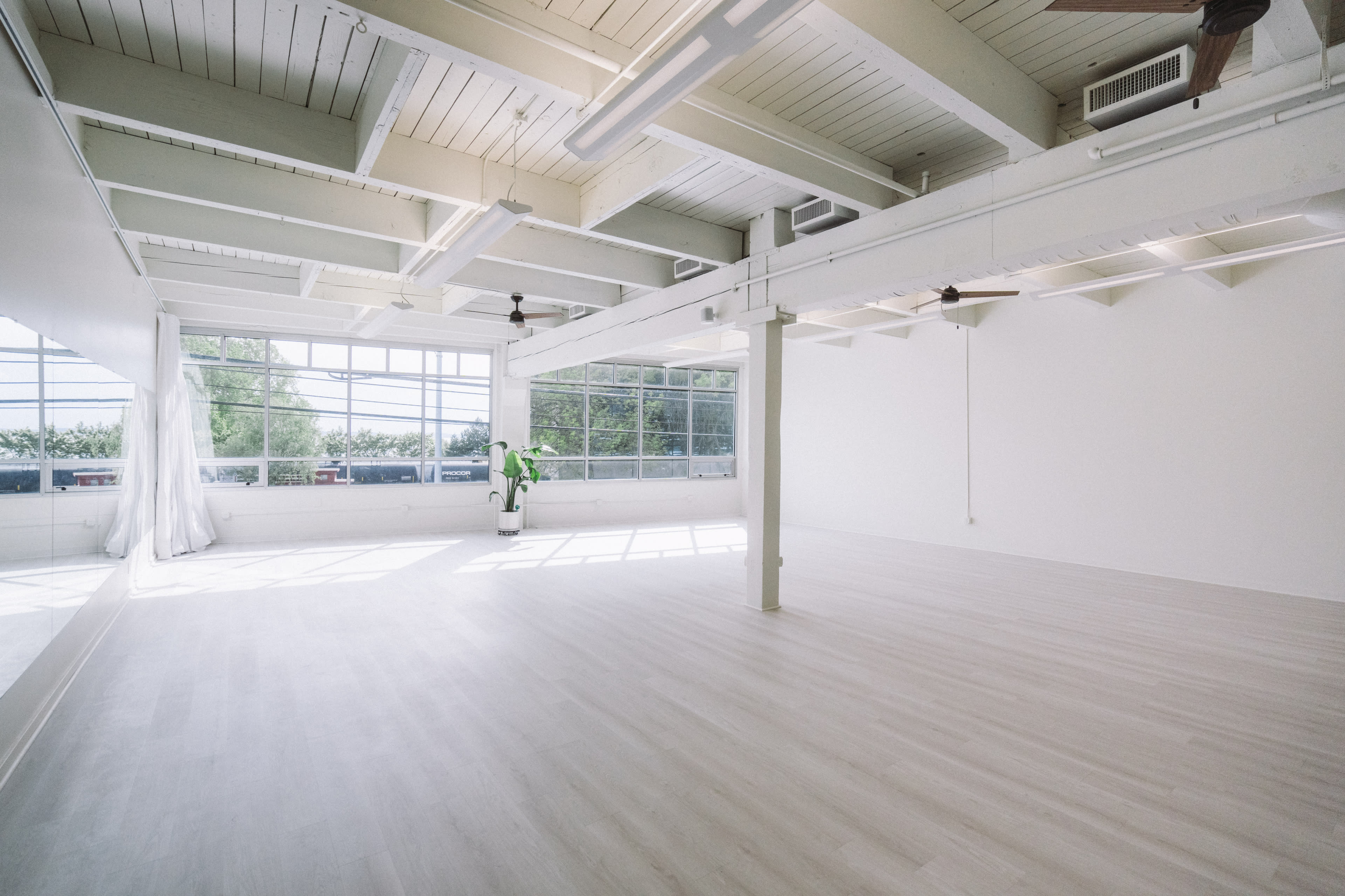 A spacious, well-lit room with large windows, light-colored flooring, and a minimalistic design.