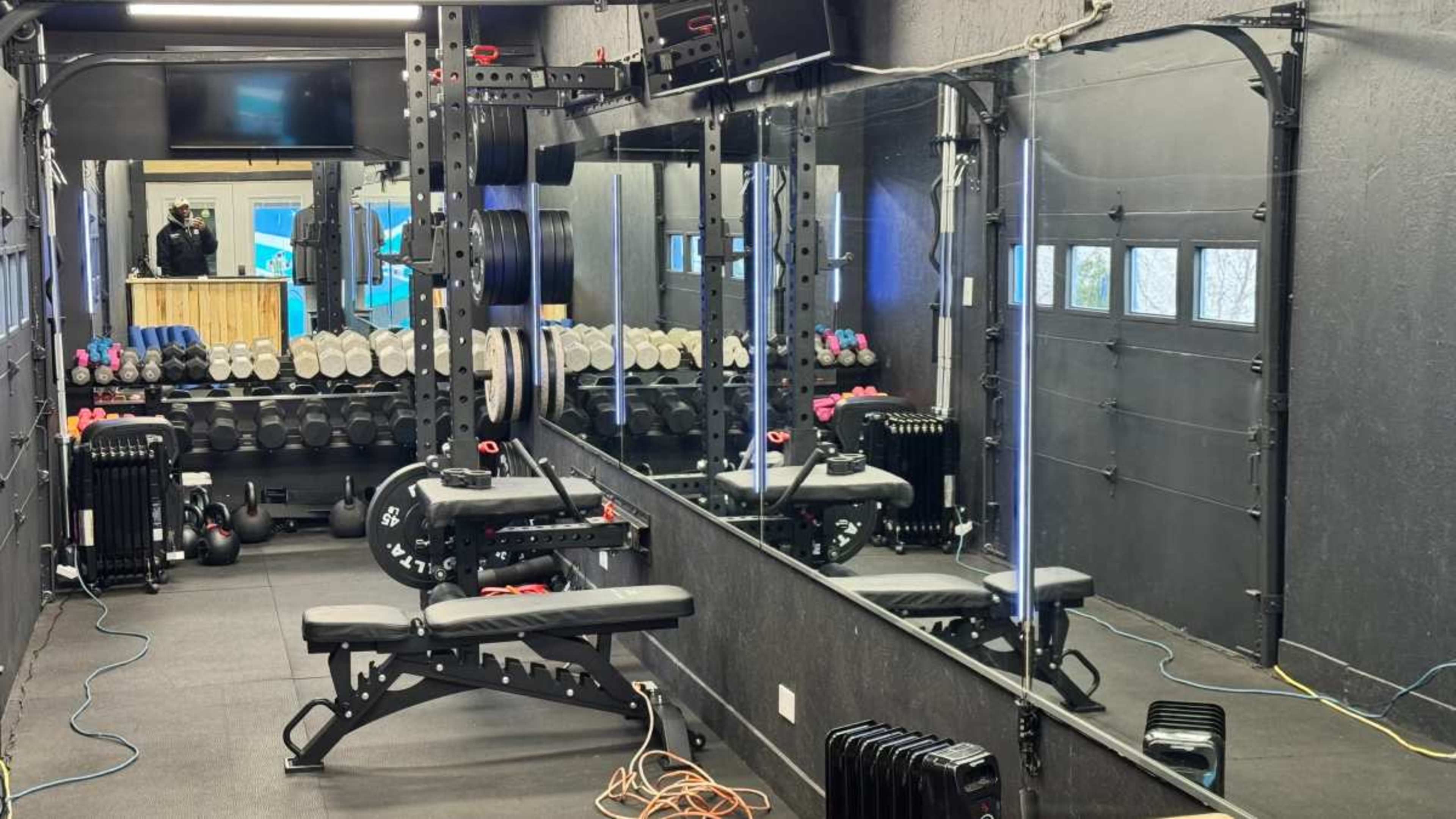 The image shows a home gym with exercise equipment, including a bench, weights, and mirrors along the wall.