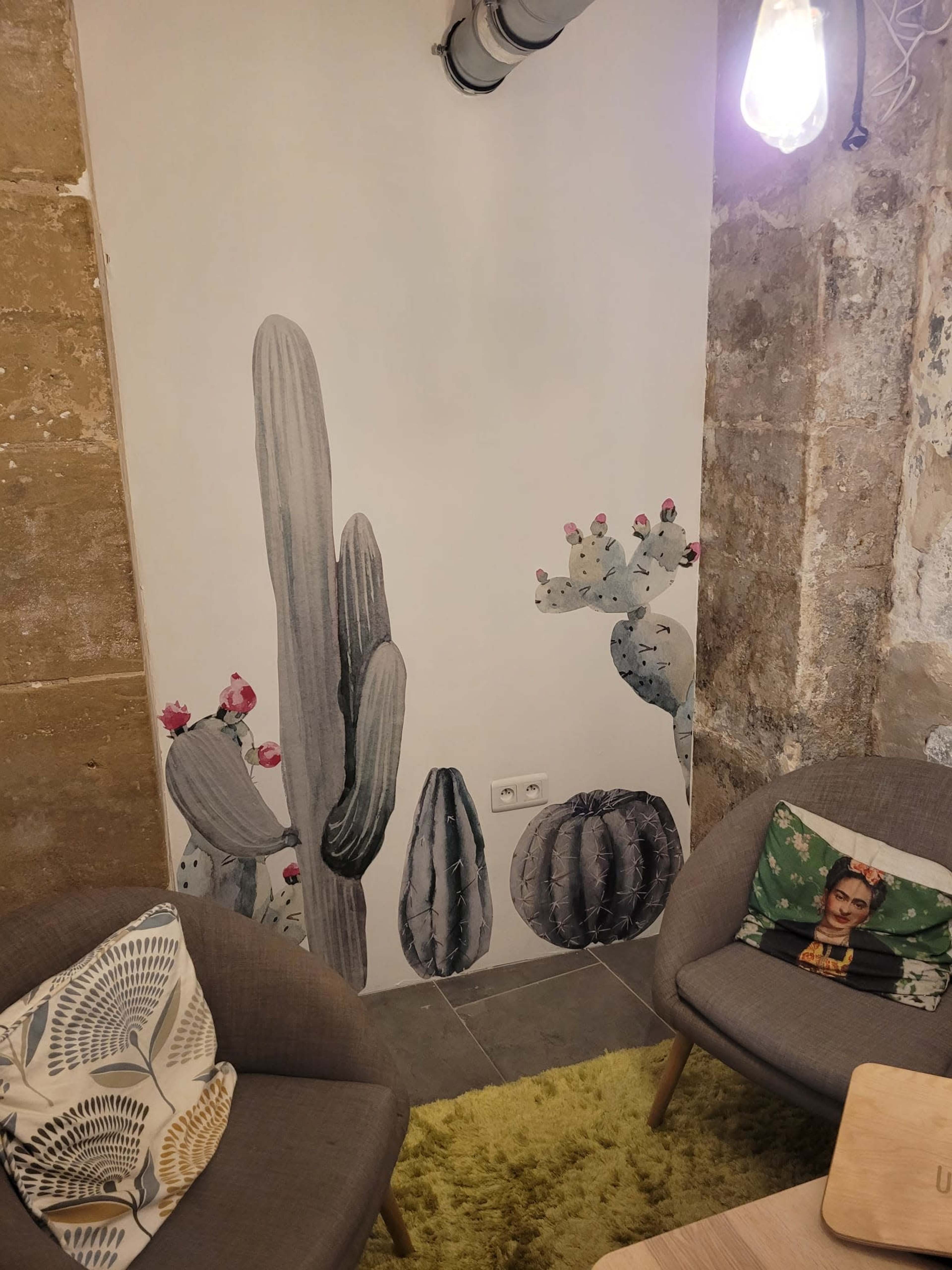A corner of a room with a textured wall featuring cactus murals and two modern chairs with decorative cushions, along with a small table.