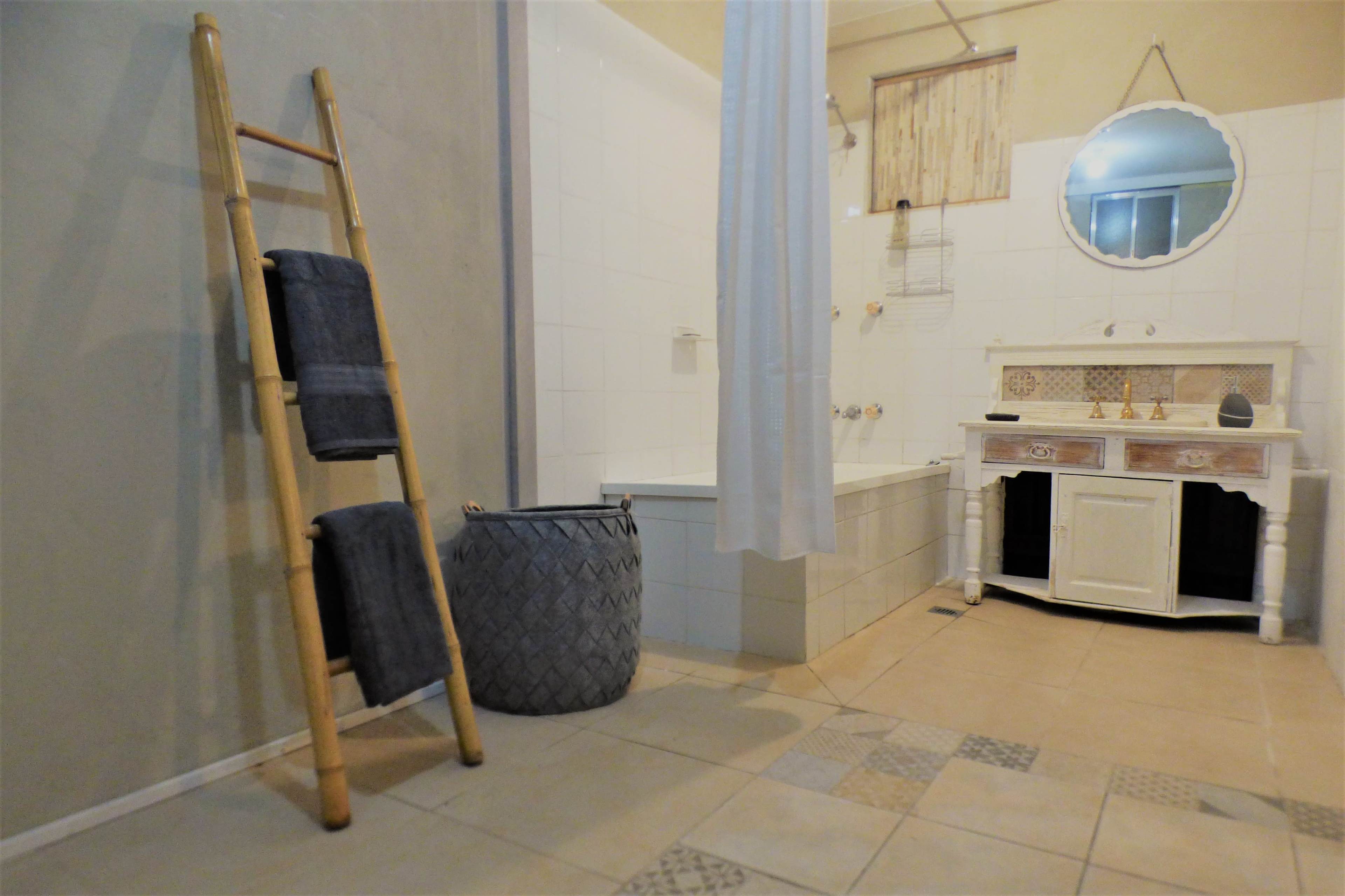 A bathroom features a bamboo towel ladder, a woven basket, and a white vintage sink cabinet beside a bathtub.