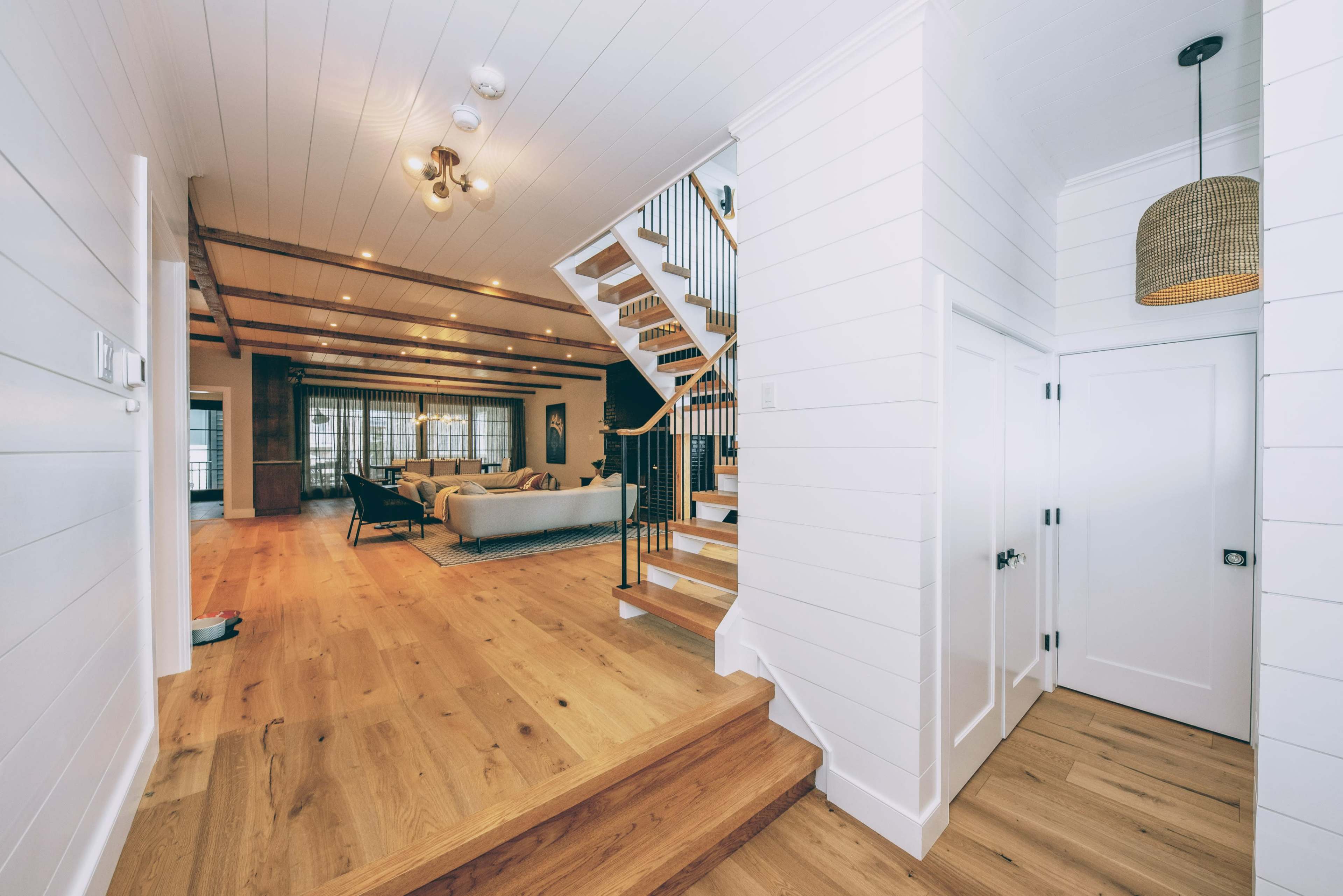 A spacious, well-lit hallway leading to a staircase and an open living area with wooden flooring and modern decor.