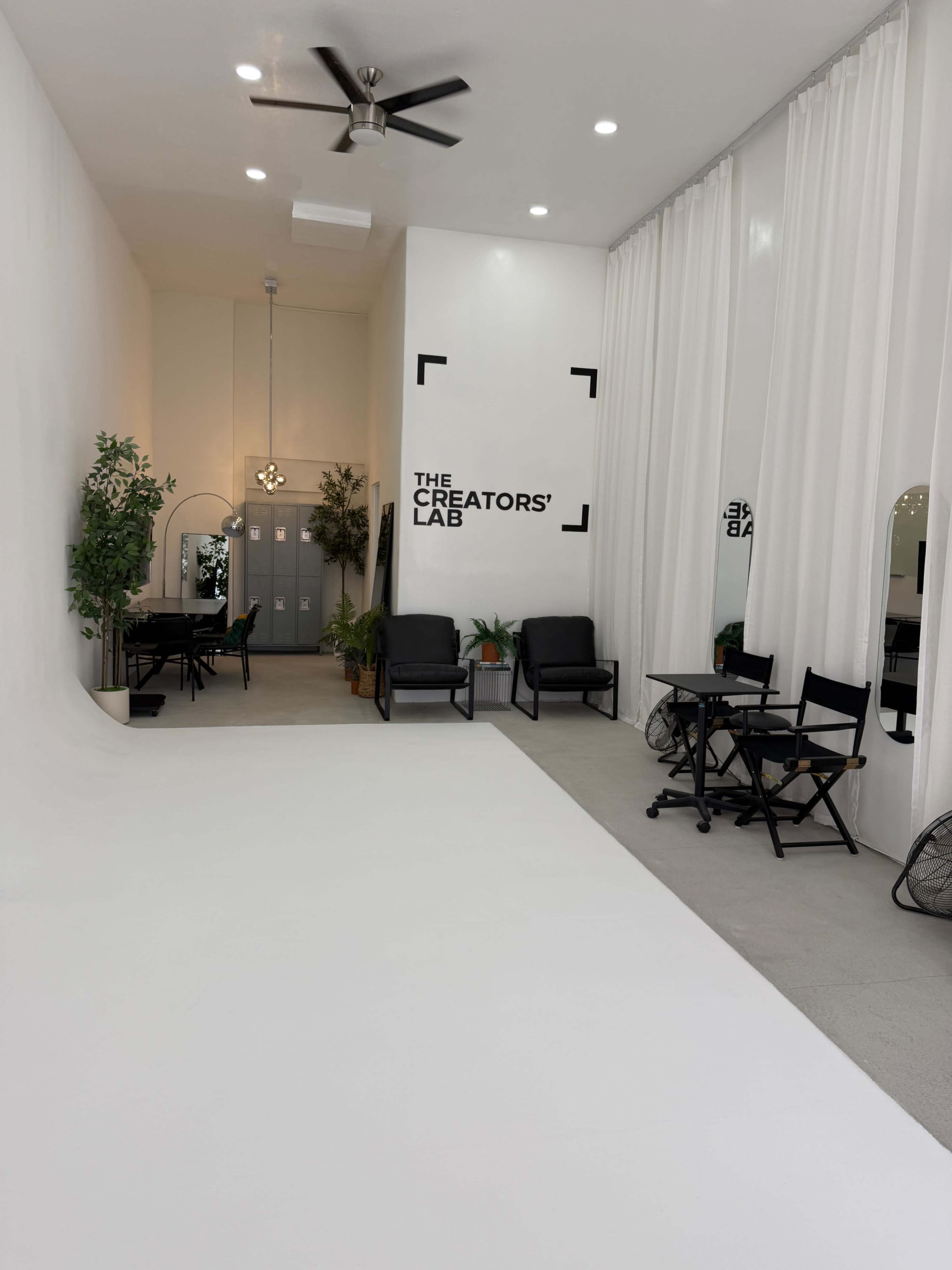 The image shows a minimalist studio space named "The Creators' Lab," featuring white walls, a white floor, and seating areas with plants and mirrors.