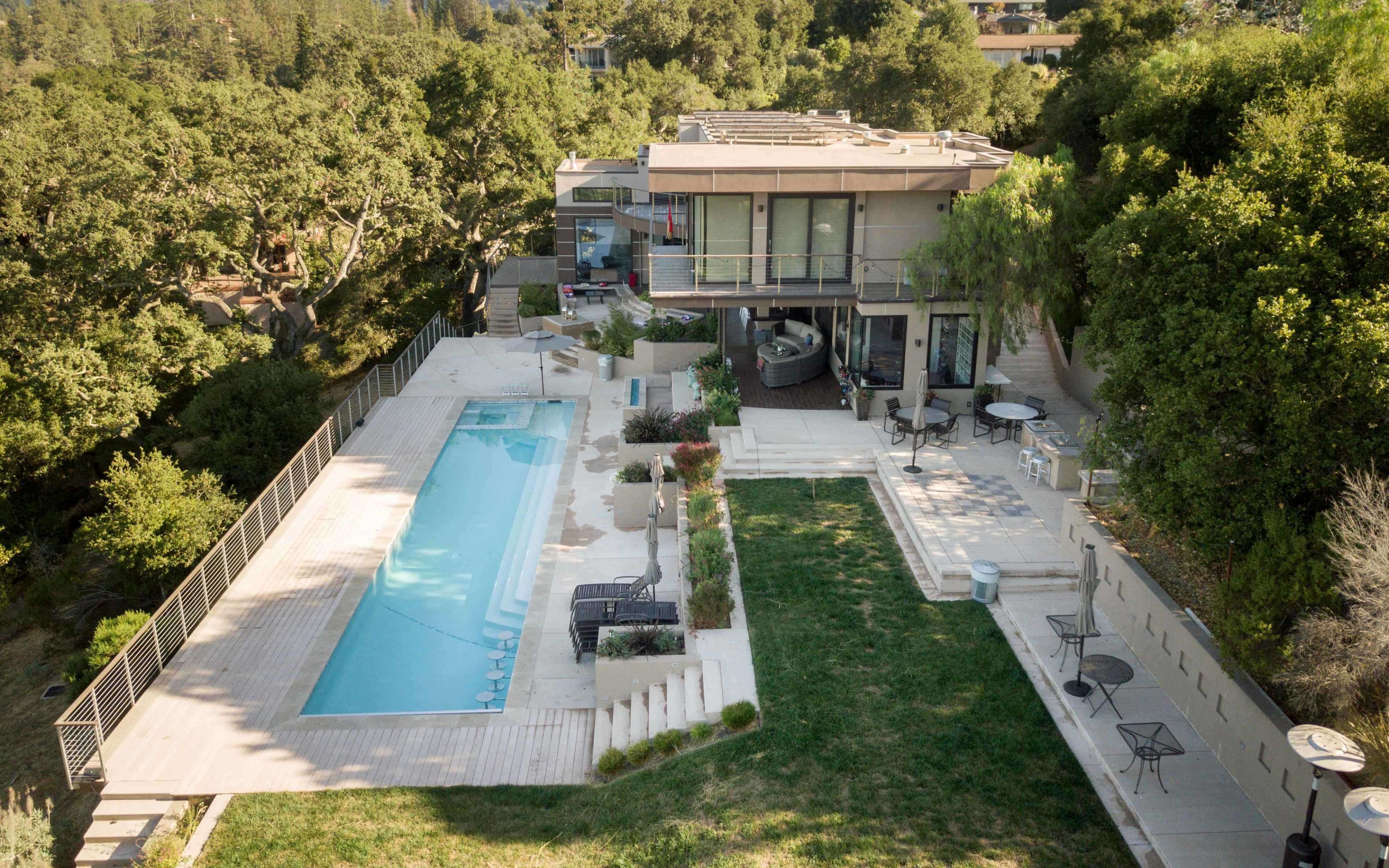 The image shows a modern house with a swimming pool and outdoor seating area surrounded by greenery.