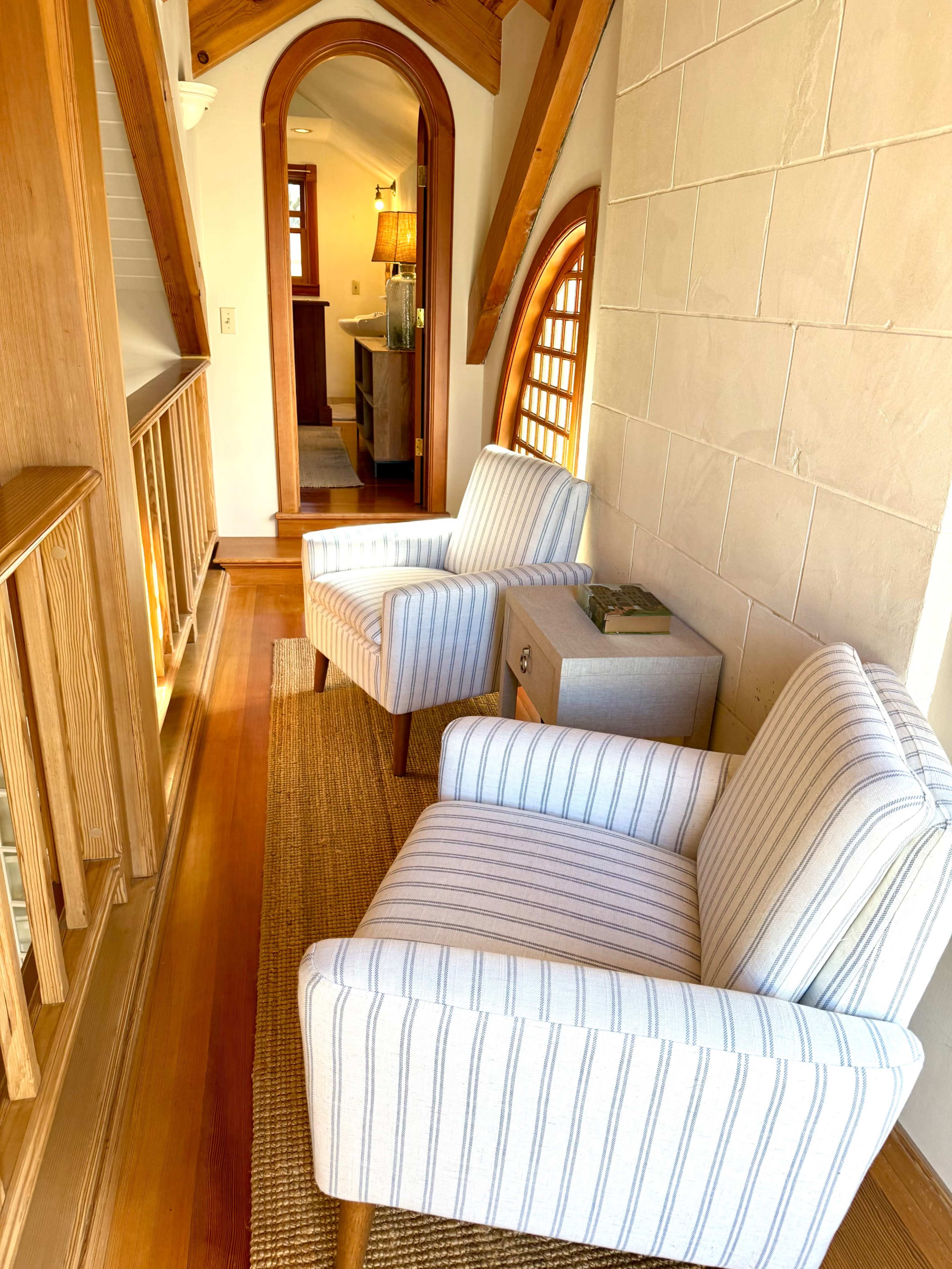 The image shows a cozy interior space featuring two striped armchairs positioned near a wooden balcony railing, with a woven rug on the floor.