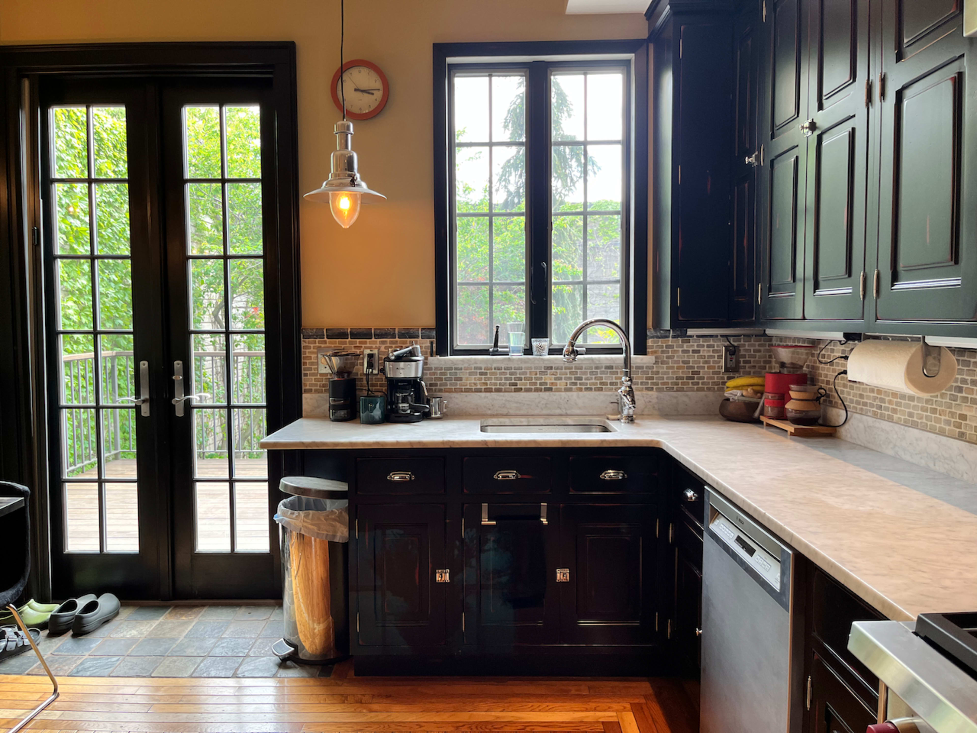 A kitchen features dark cabinetry, a stainless steel sink, and a large window overlooking a deck.