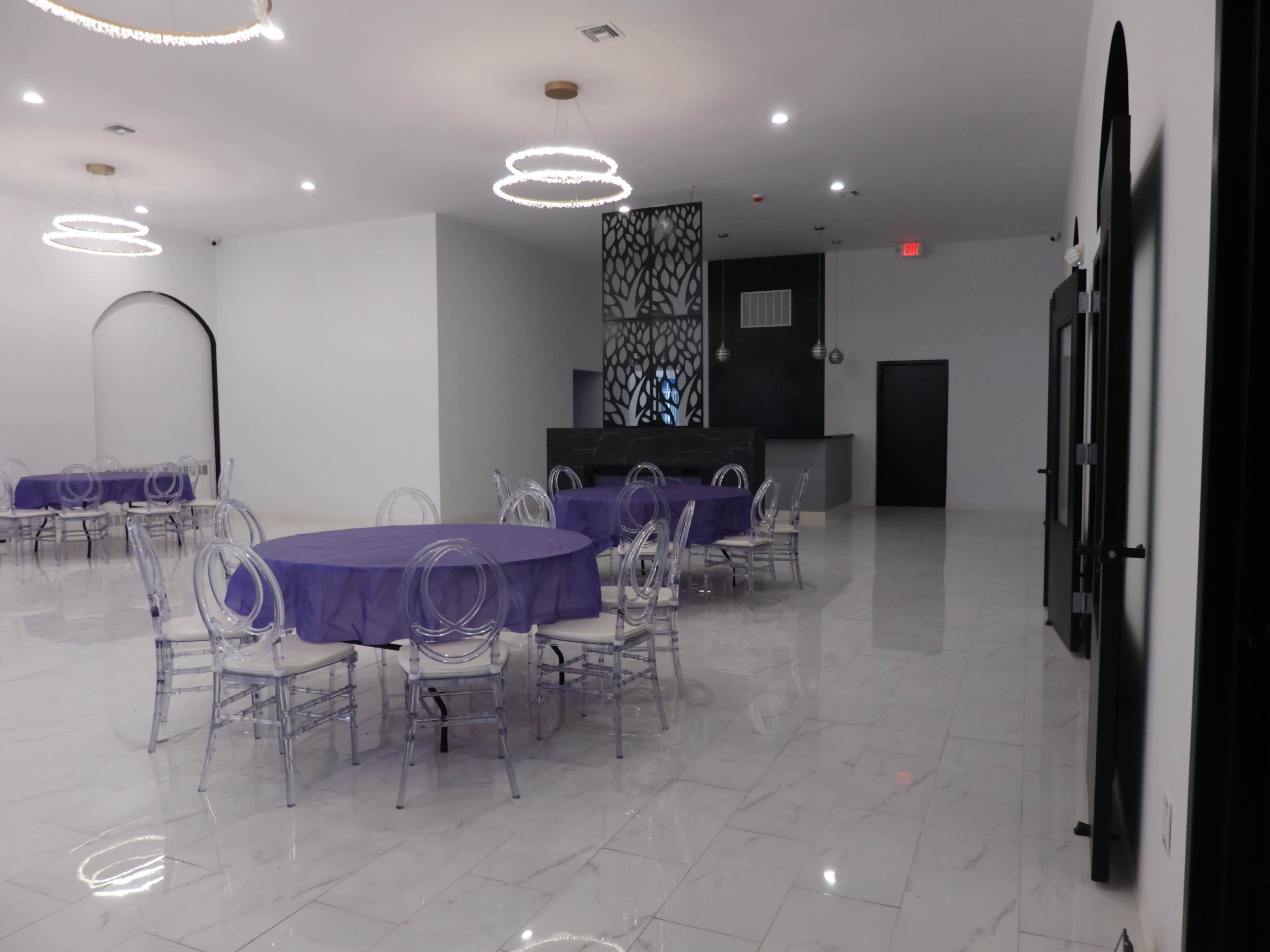 An empty event space with purple tablecloths on circular tables and a modern reception area in the background.
