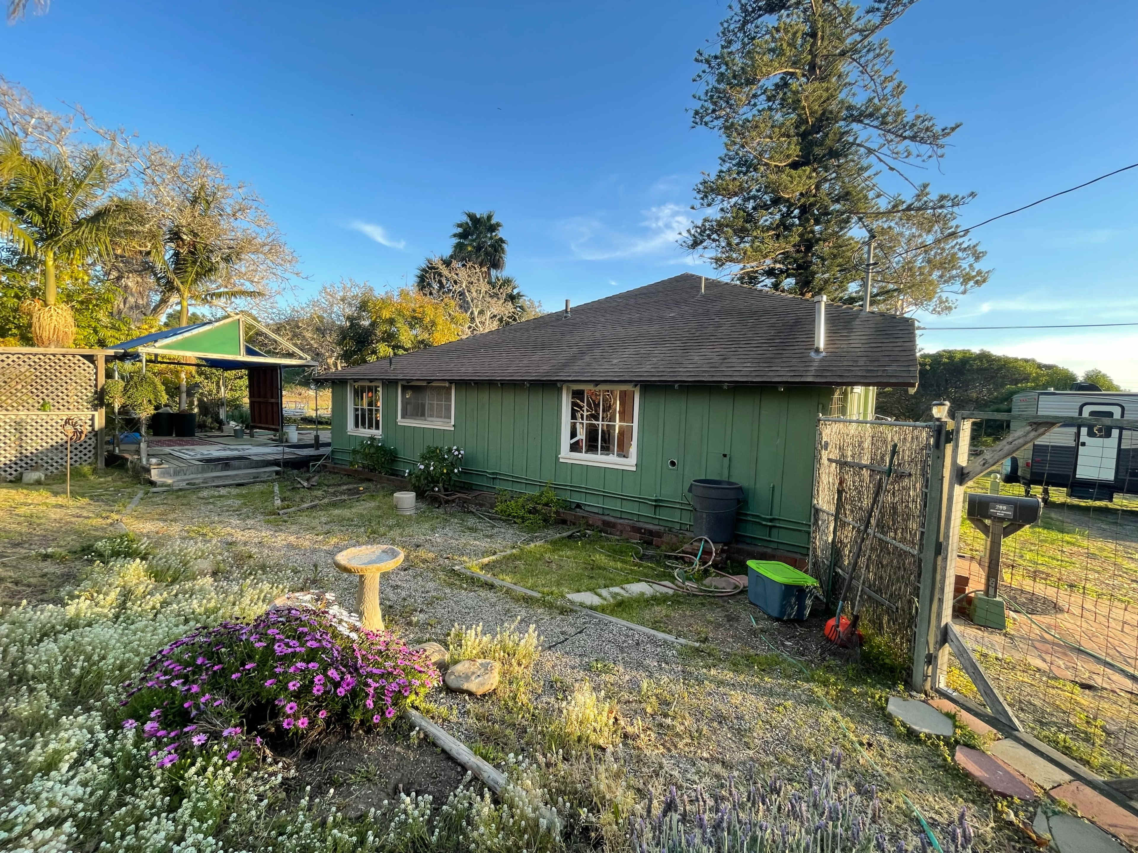 A green house with a sloped roof surrounded by a landscaped yard featuring flowers and a gravel path.