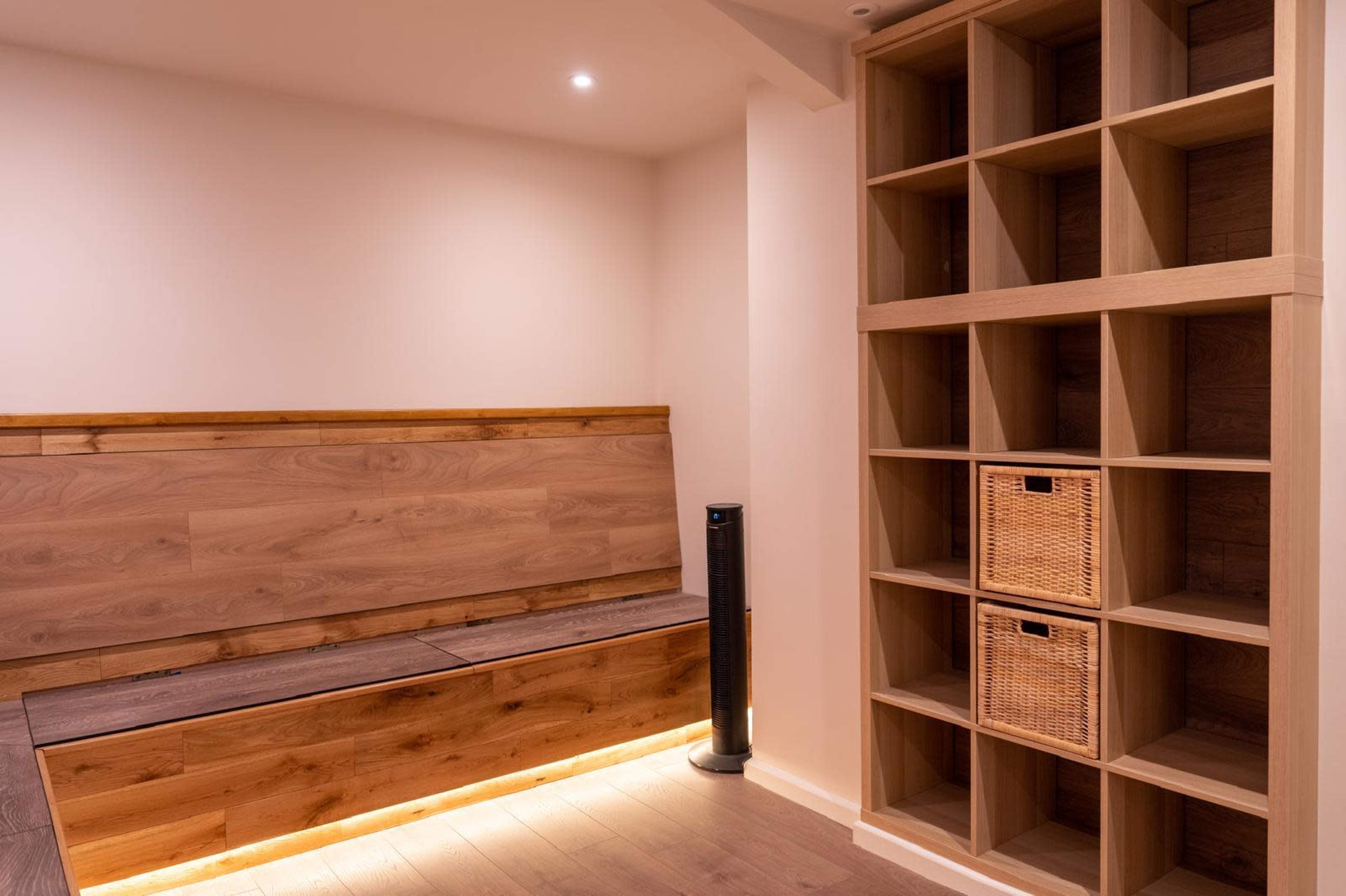 The image shows a minimalist room featuring a wooden storage bench and a shelving unit with woven baskets.