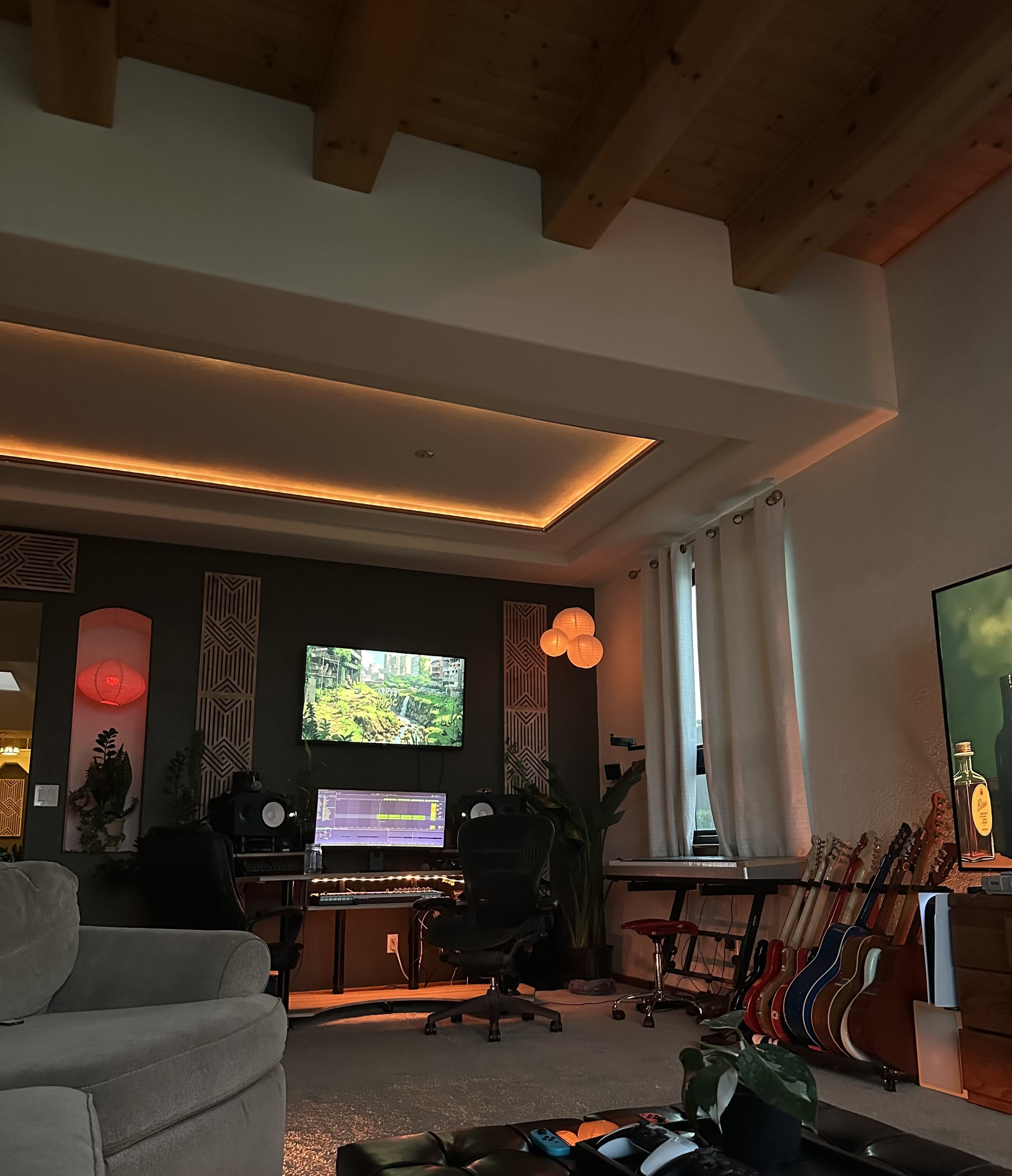 The image shows a cozy music studio filled with musical instruments, a computer setup with multiple monitors, and soft ambient lighting.