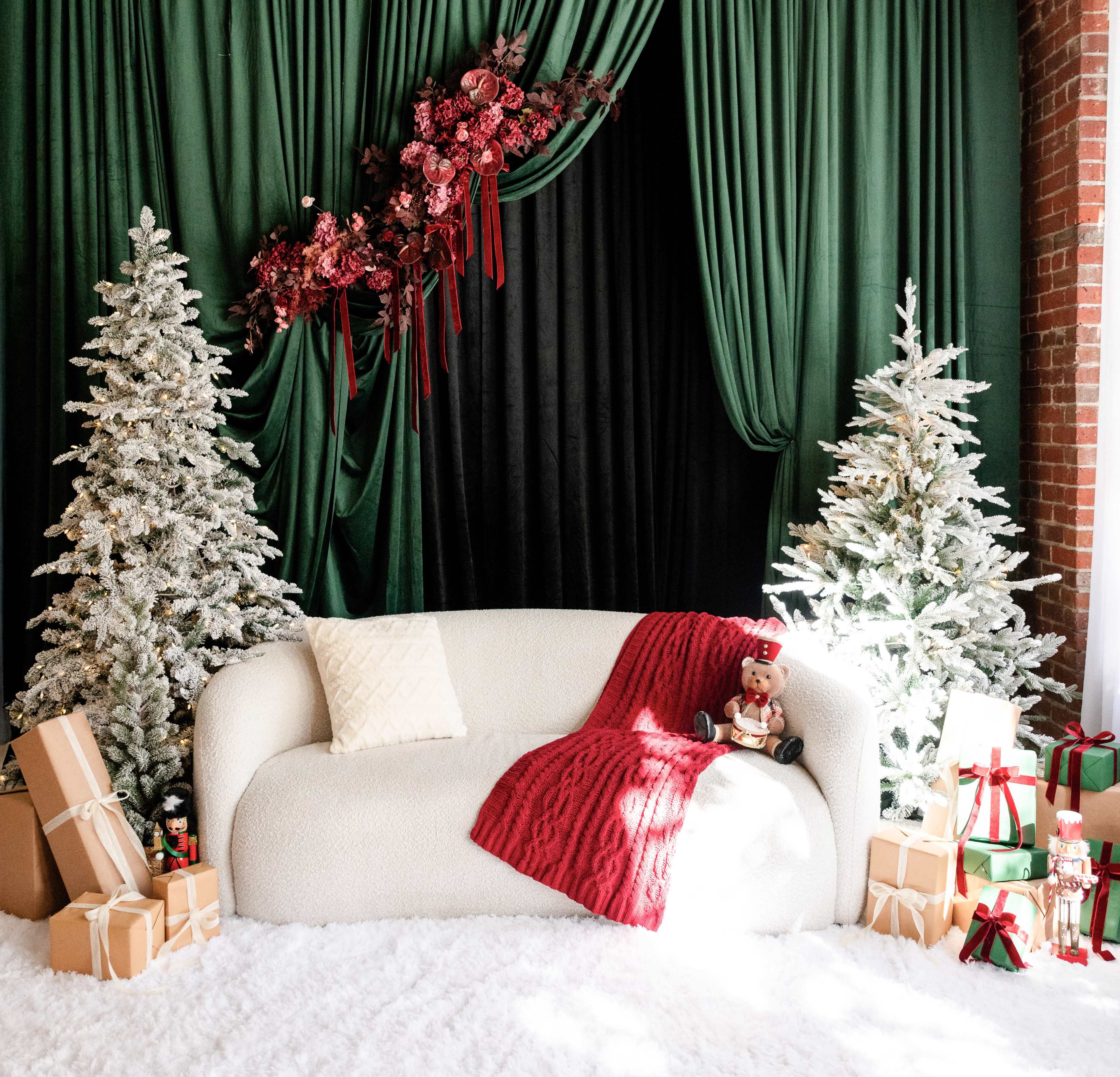 The image features a cozy living room scene with a white sofa draped in a red blanket, flanked by two frosted Christmas trees and surrounded by neatly wrapped gifts.