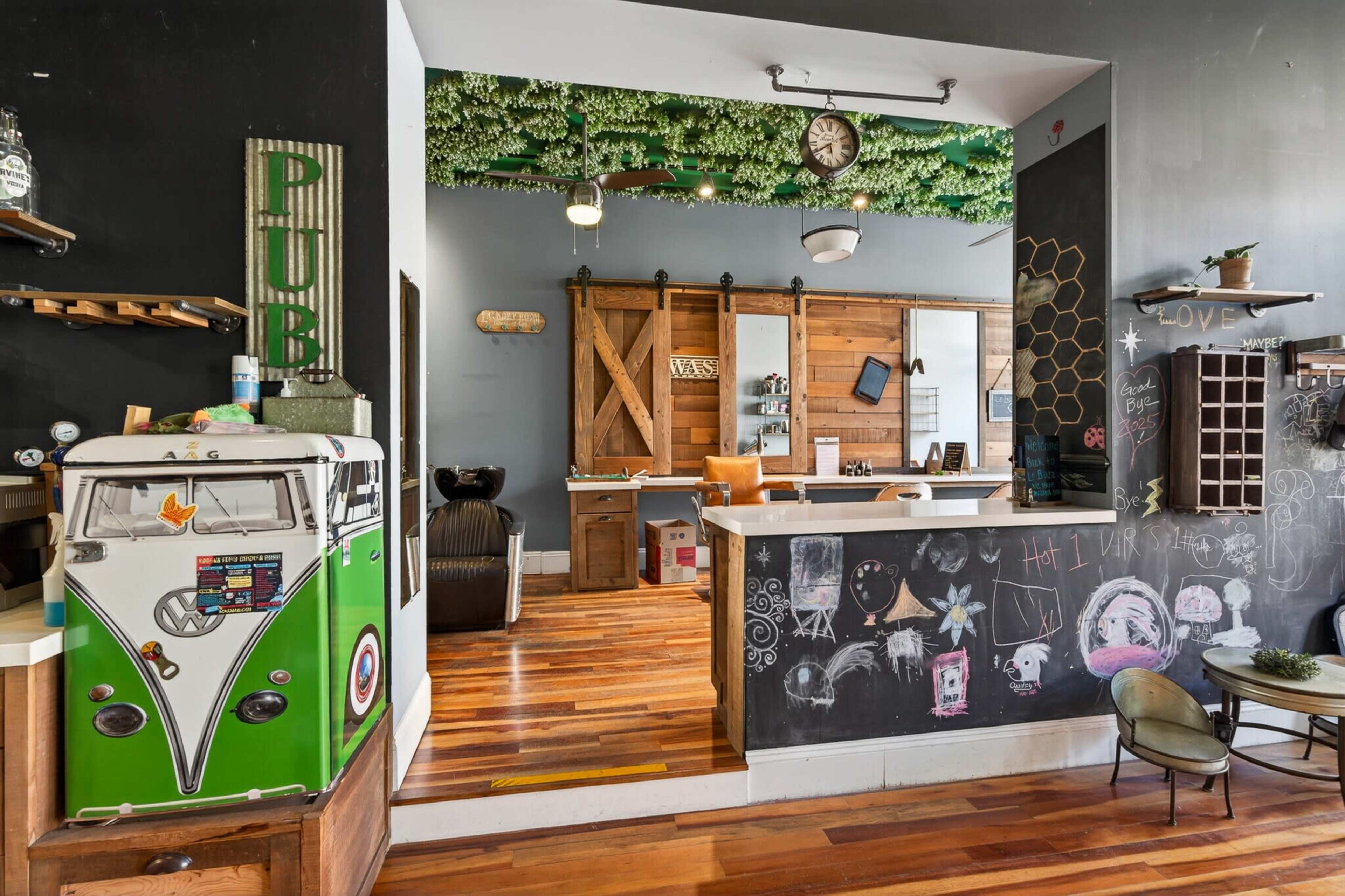 The image depicts a vibrant indoor space featuring a bar area with wooden accents, a chalkboard wall, and decorative greenery overhead.