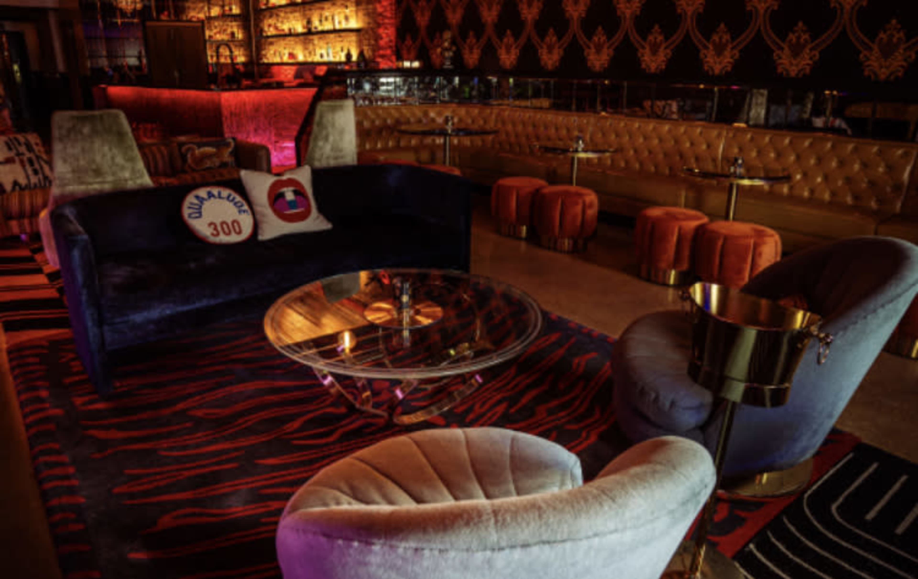 A stylish lounge area with a plush velvet sofa, two upholstered chairs, a glass coffee table, and a patterned rug, all set against an elegantly decorated backdrop.