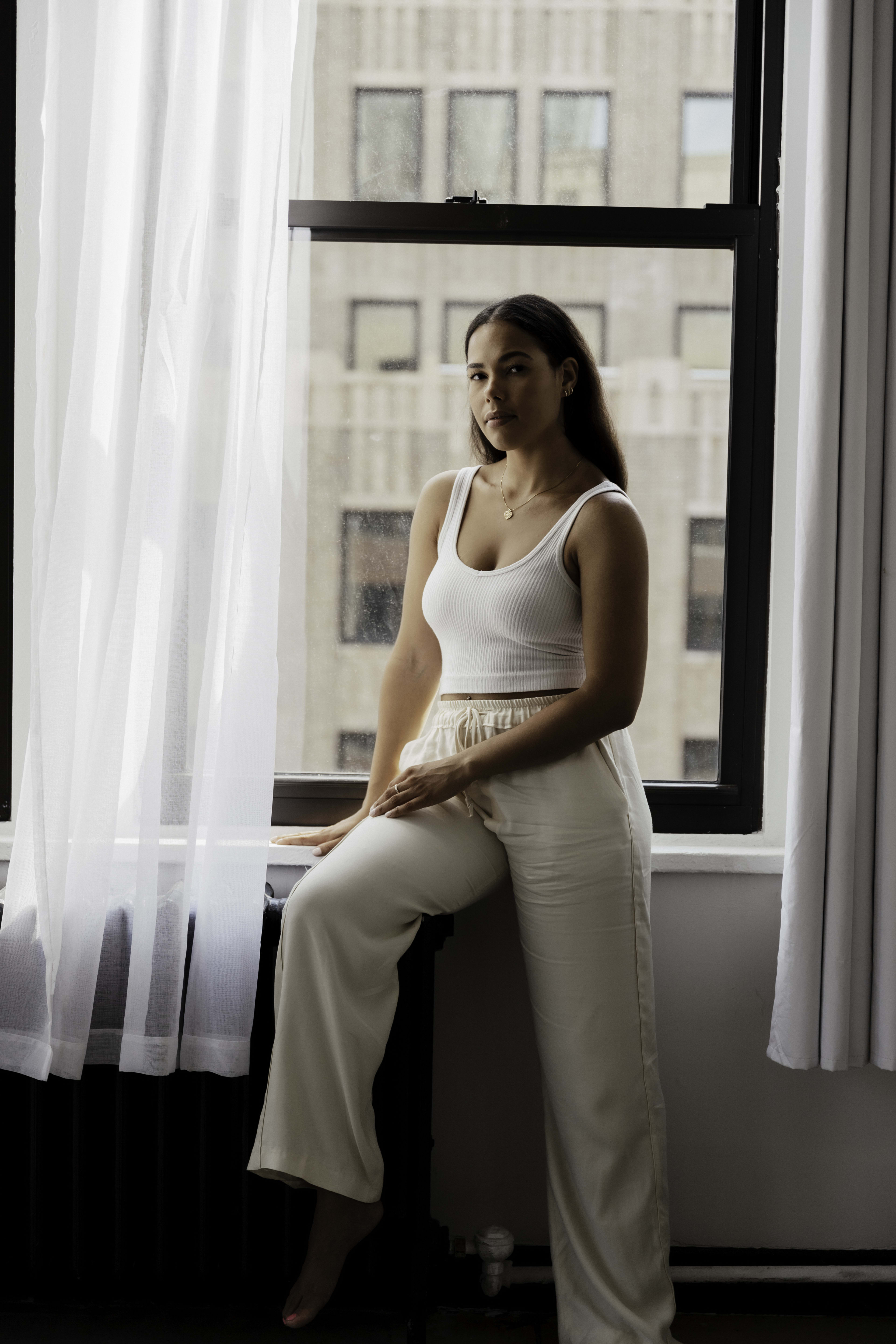 A fashion photoshoot featuring a woman on a minimal white window sill.