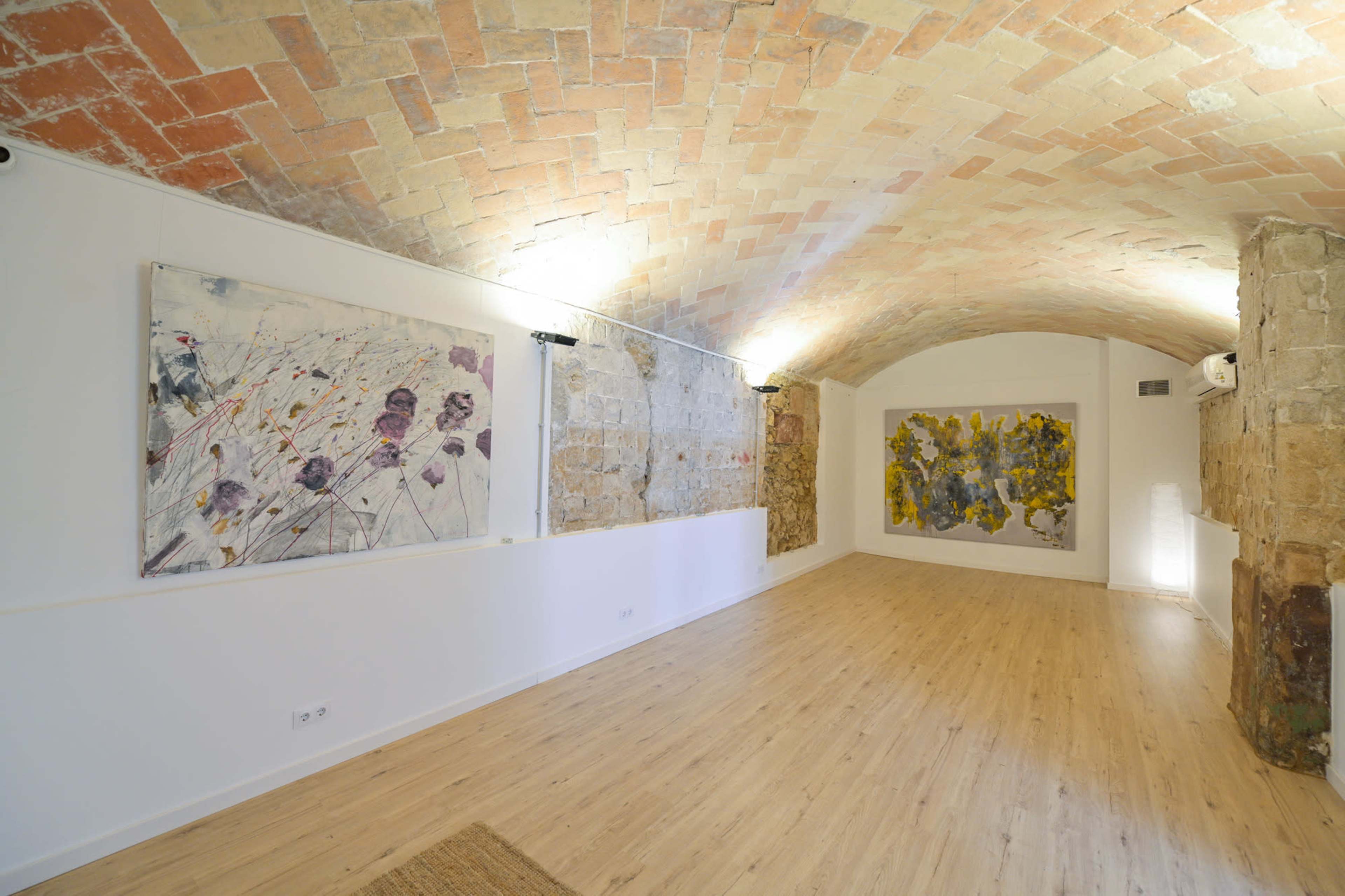 The image shows an art gallery with a curved brick ceiling, featuring two large paintings on the walls and wooden flooring.