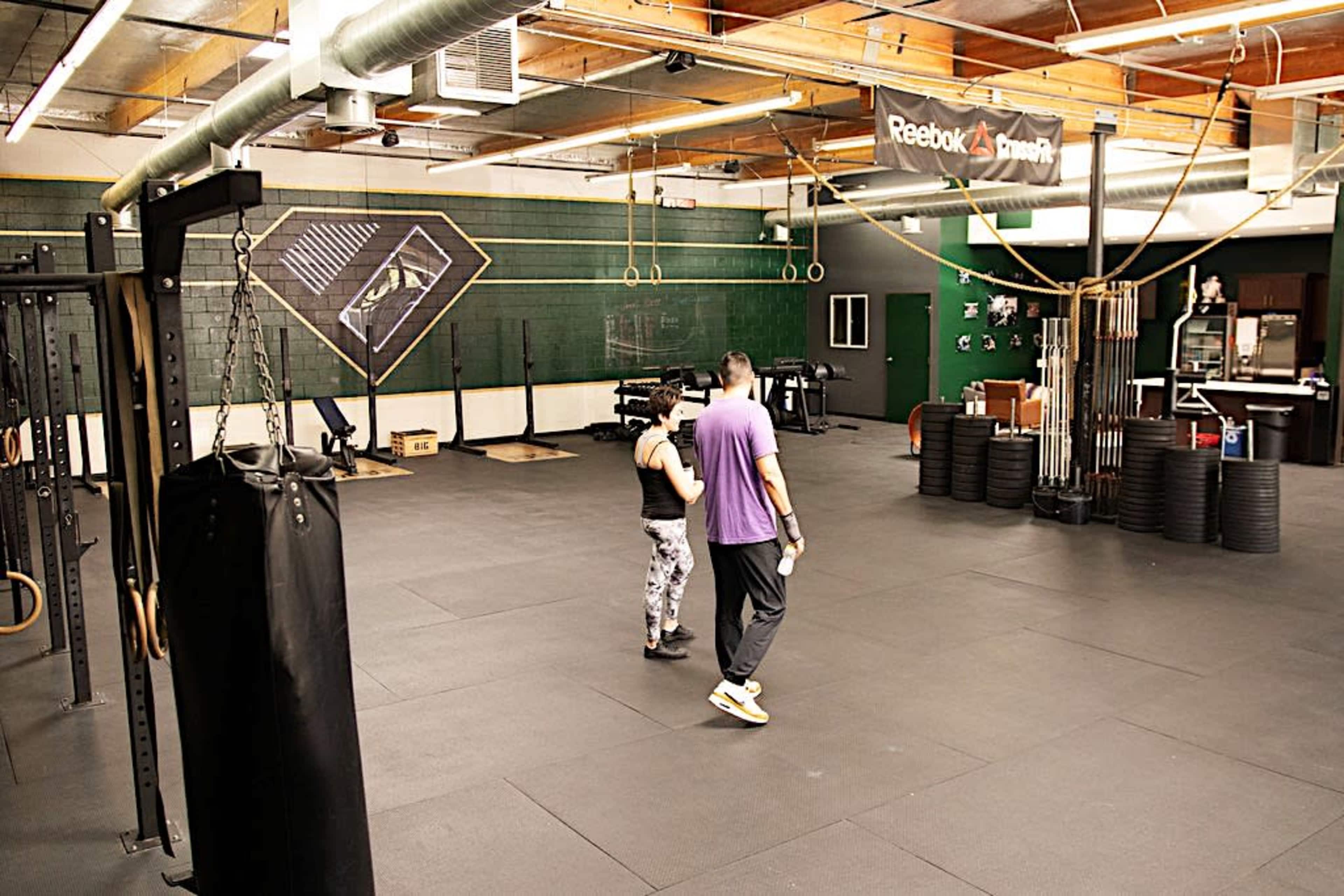 A person in workout attire is guiding another individual through an exercise routine in a spacious gym with various fitness equipment.