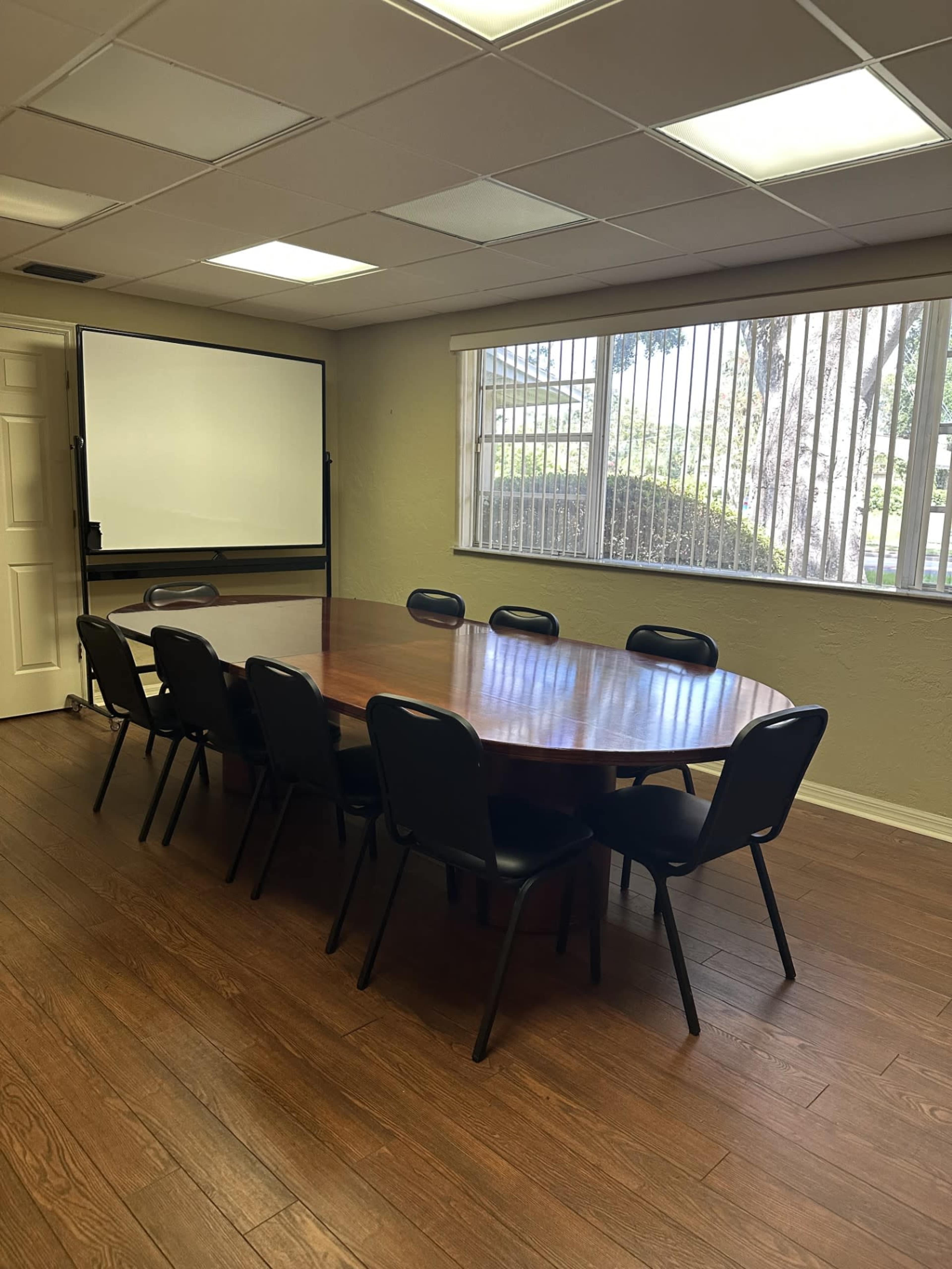 A conference room with a large oval wooden table surrounded by black chairs and a projector screen at the front.