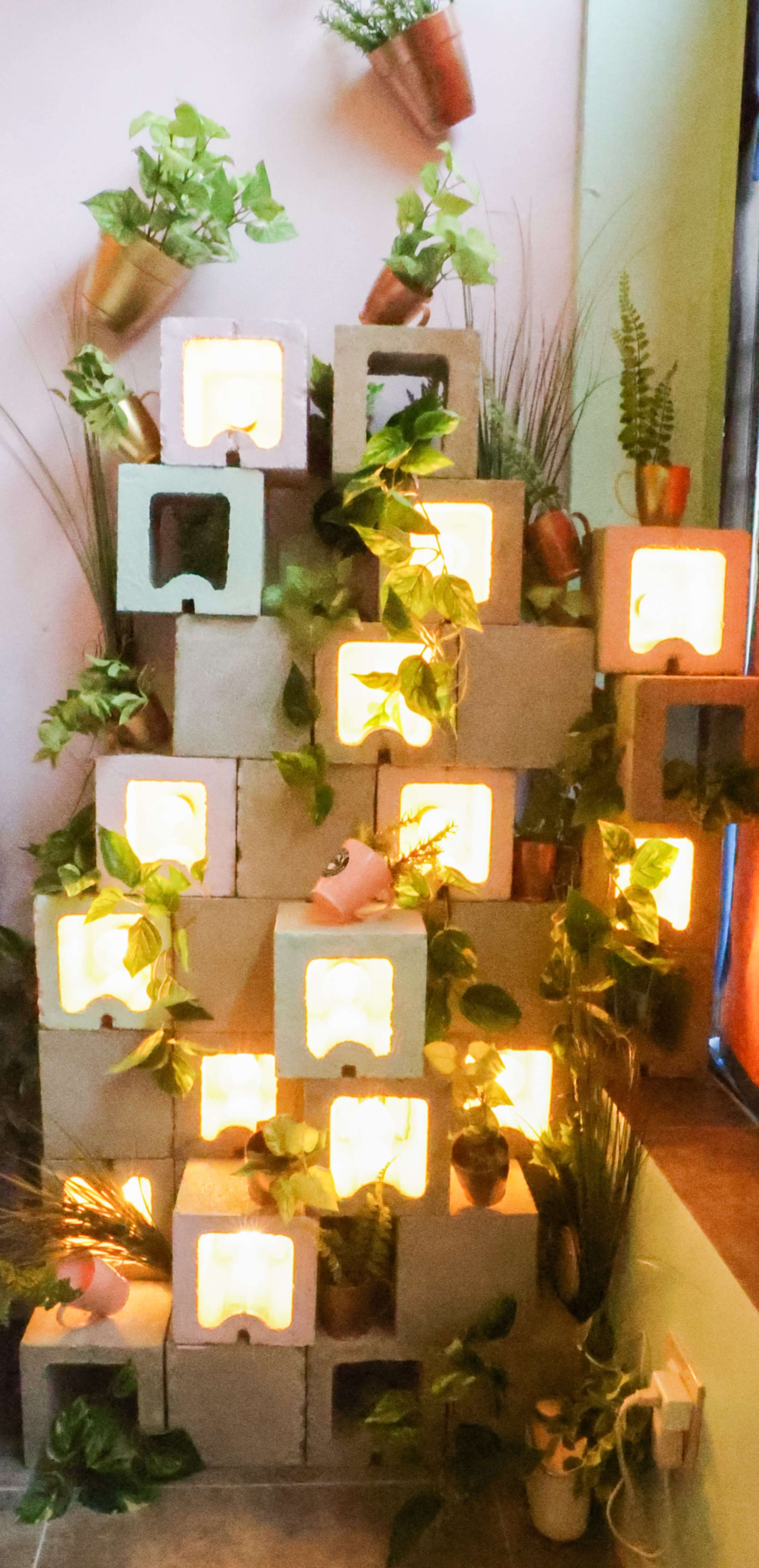 A decorative arrangement of concrete blocks illuminated from within, adorned with potted plants and greenery.