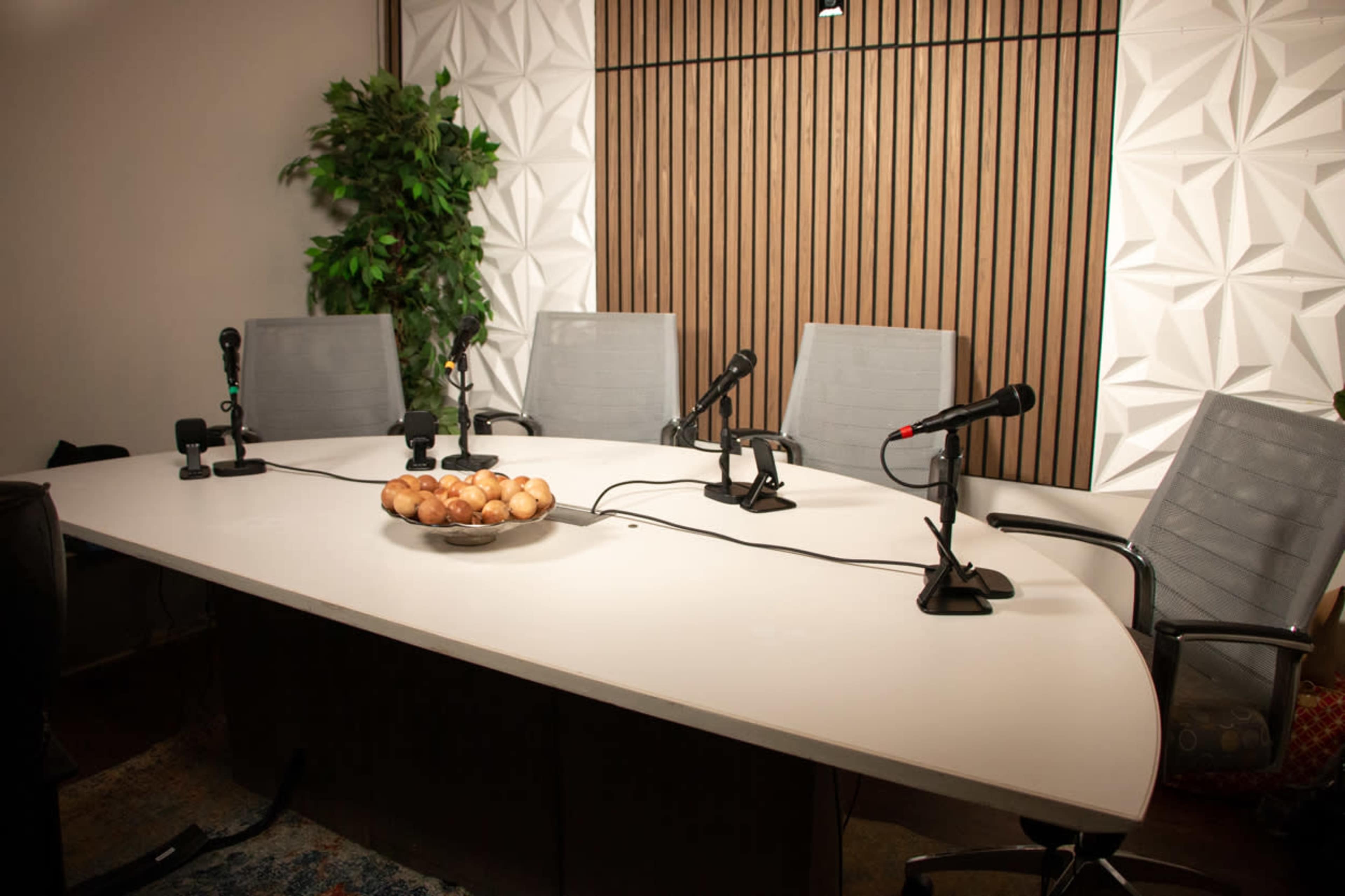 A modern conference room featuring a large white table with microphones, chairs, and a bowl of eggs as a centerpiece.