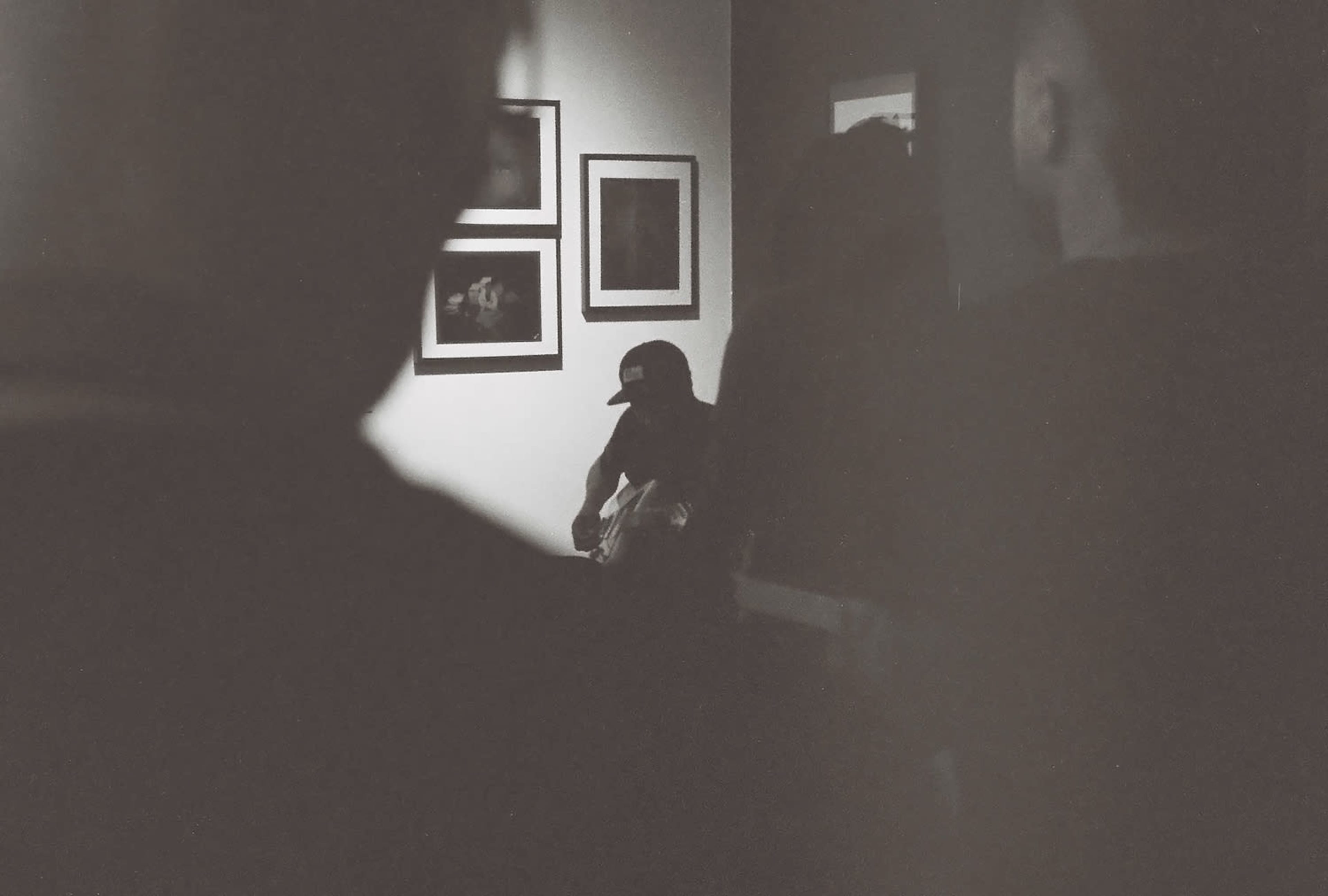 A musician sits in a dimly lit space, playing an instrument surrounded by shadowy figures.