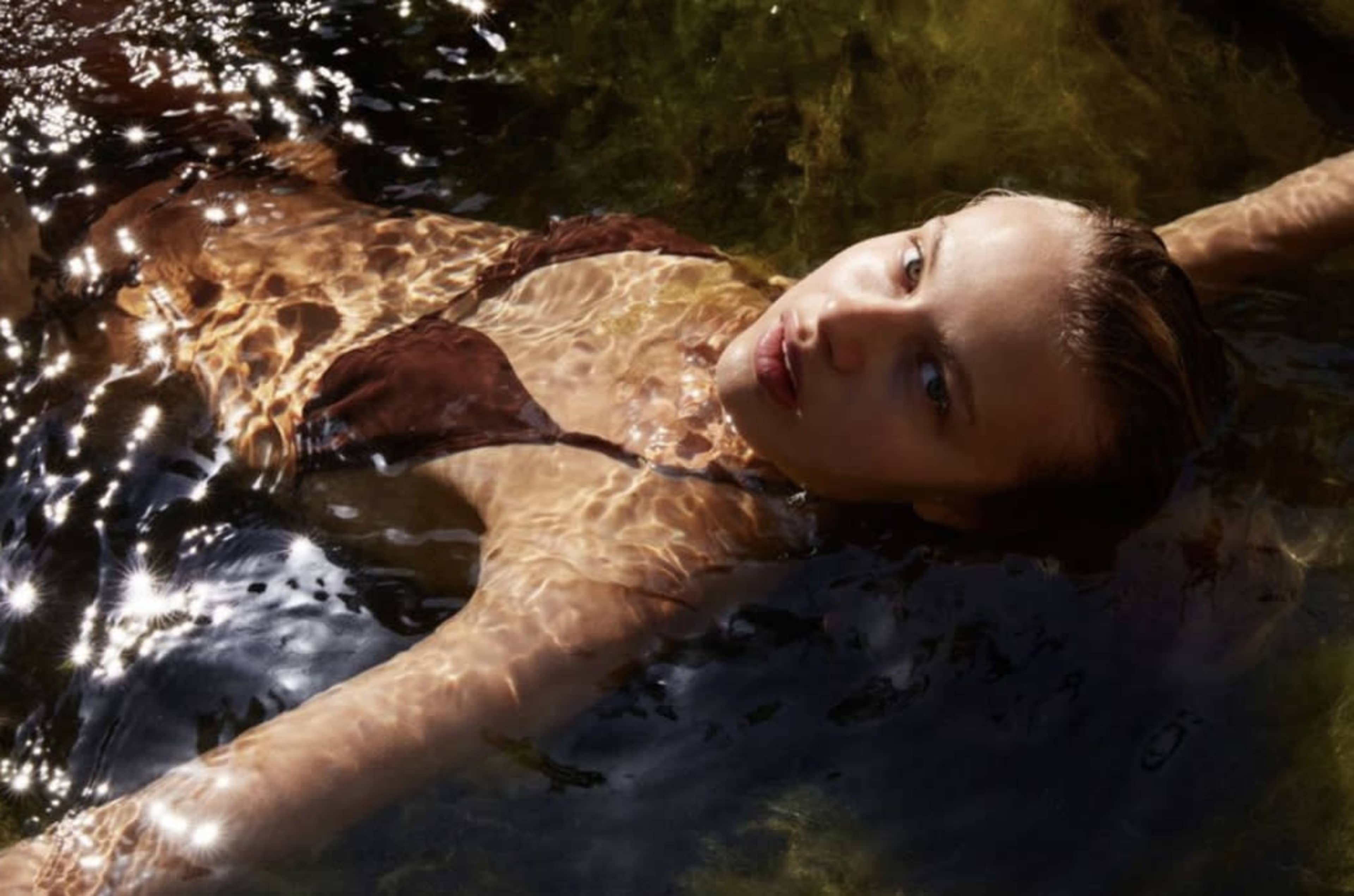 A person floats in water, surrounded by rippling reflections of light and green algae.
