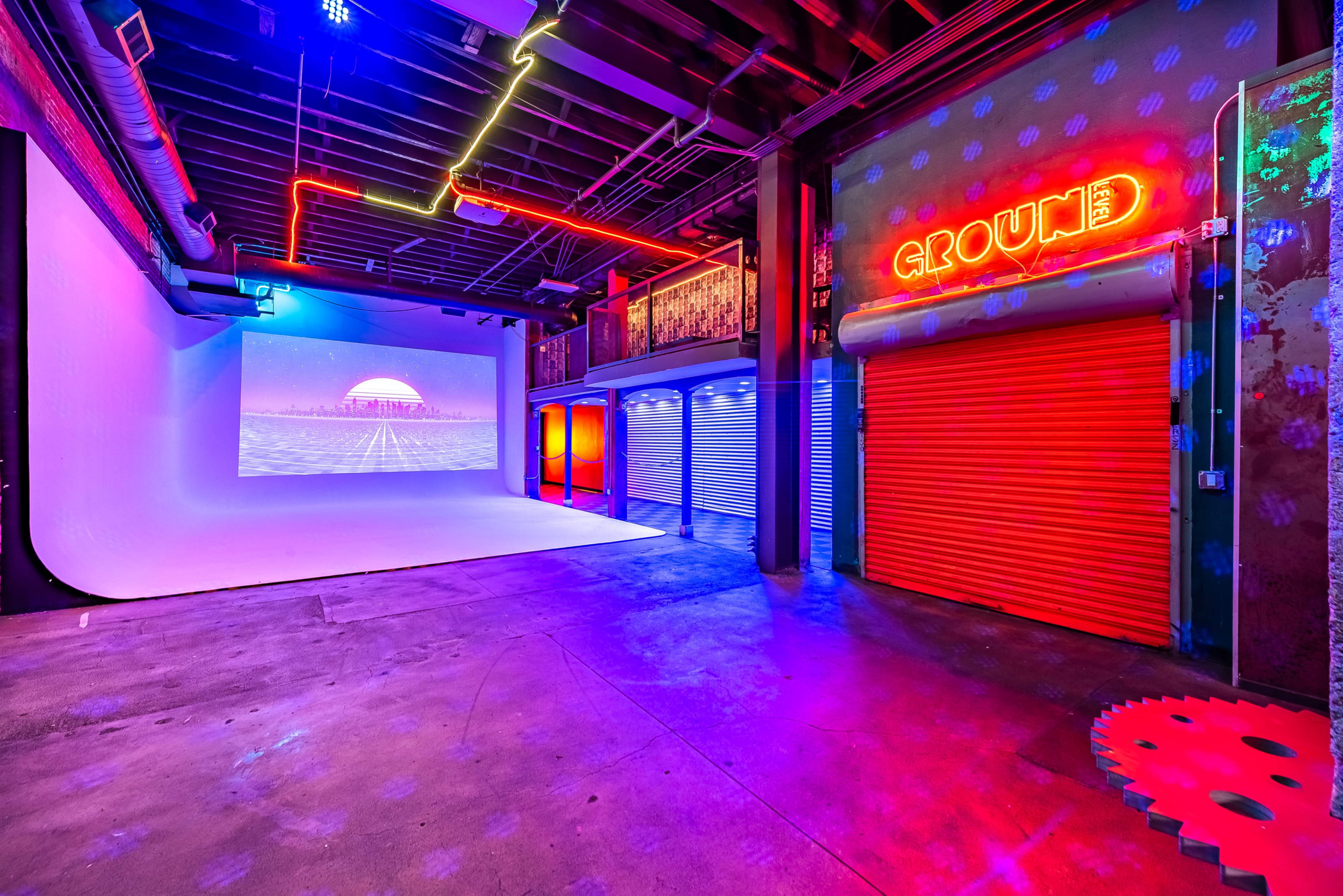A vibrant studio with neon lights, including a "GROUND" sign, and a screen displaying a sunset over water.