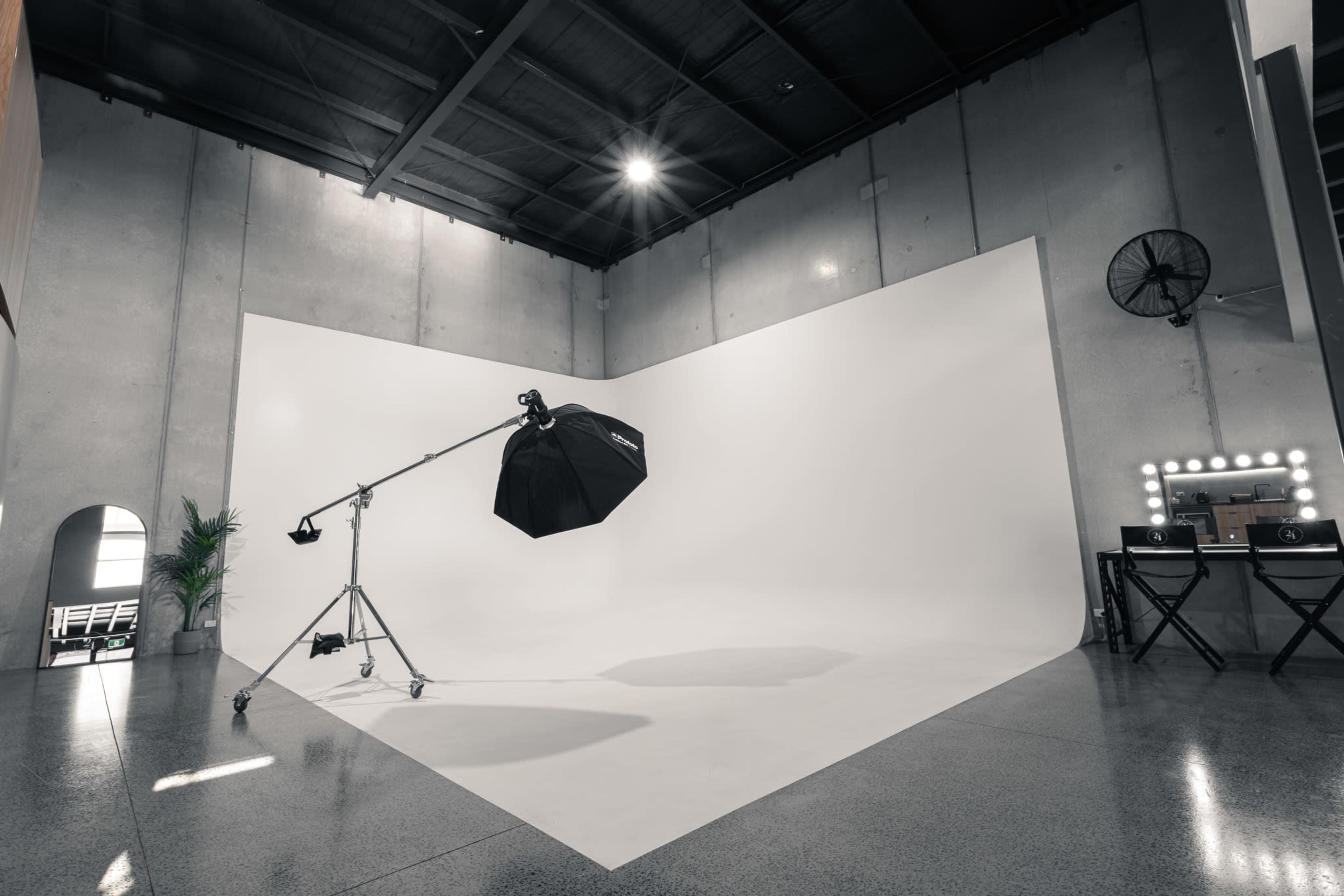 A spacious photography studio with a large white backdrop, lighting equipment, and a vanity mirror setup.