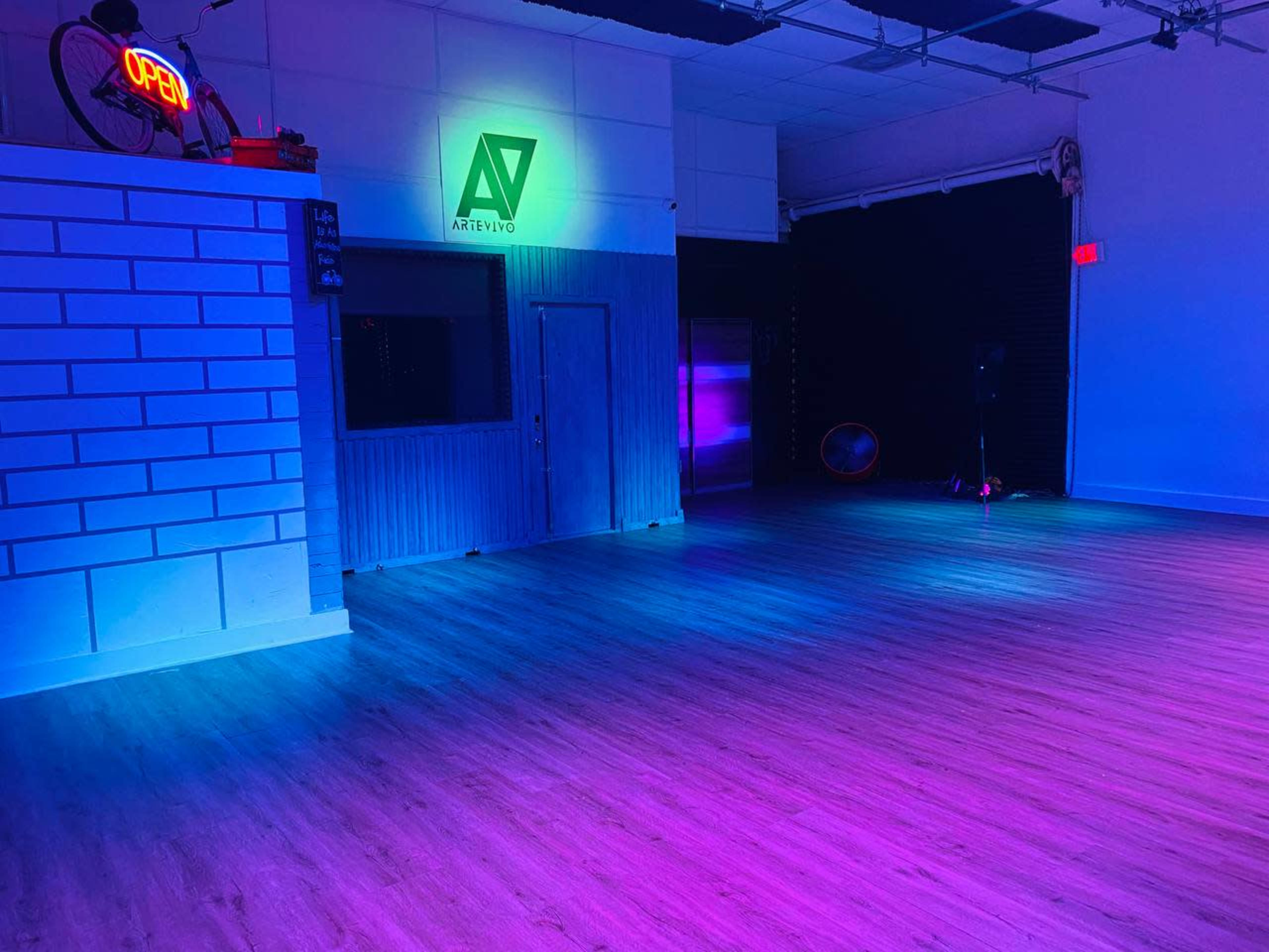 The interior of a dance studio features a large open space with wooden flooring illuminated by multicolored LED lights.