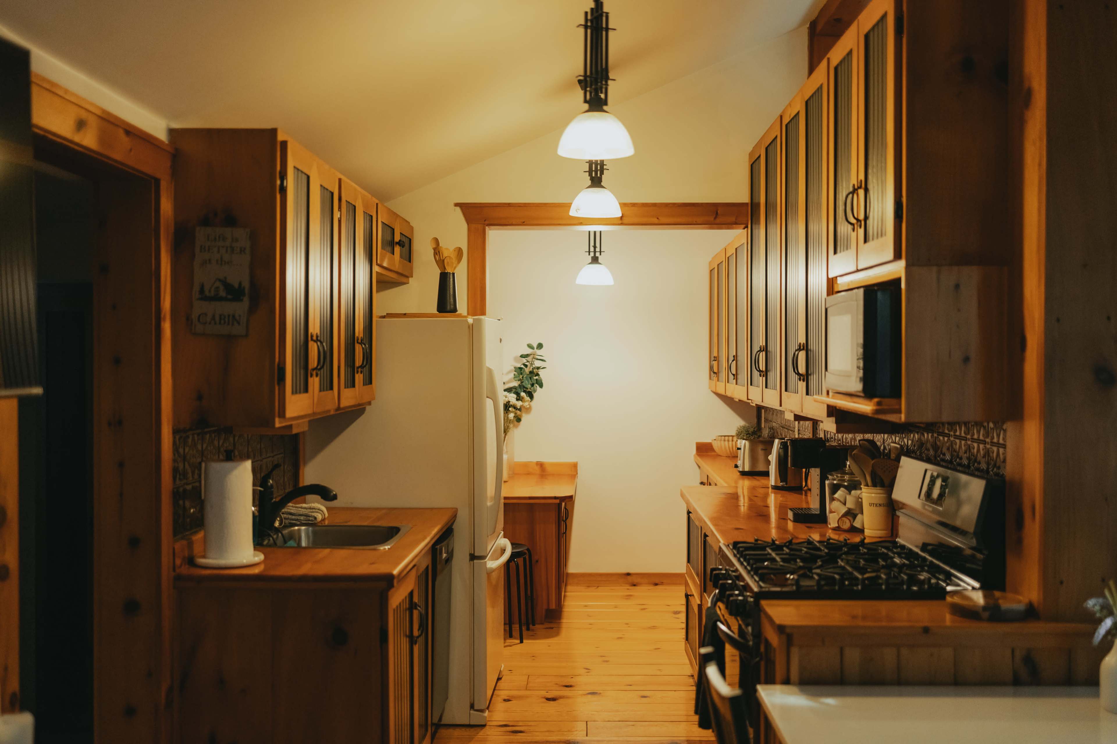 The kitchen features wooden cabinetry, a white refrigerator, and a central island with a stove, illuminated by pendant lighting.