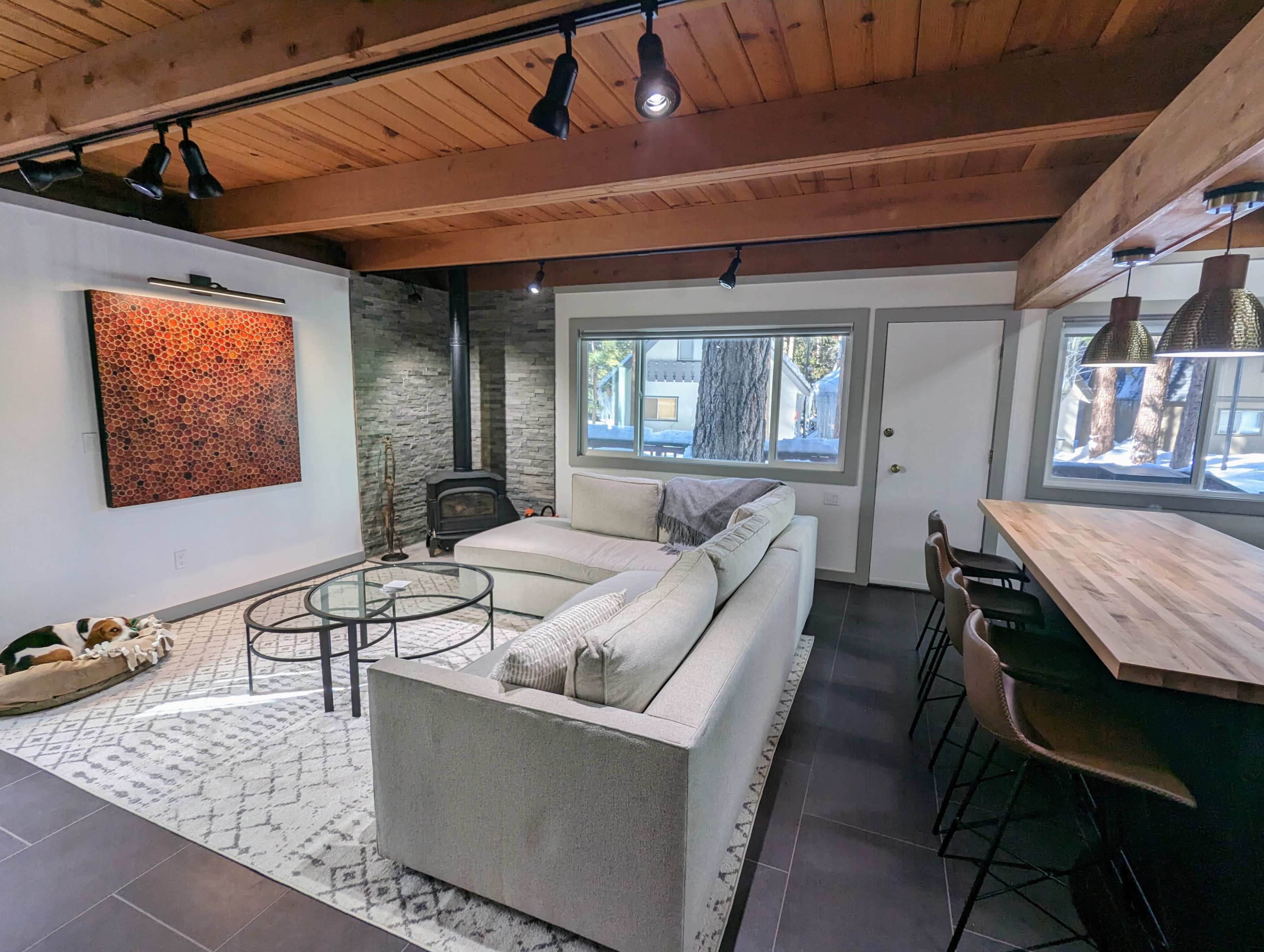 A modern living room with a sectional sofa, a glass coffee table, a stone fireplace, and a dining area featuring a wooden counter with bar stools.