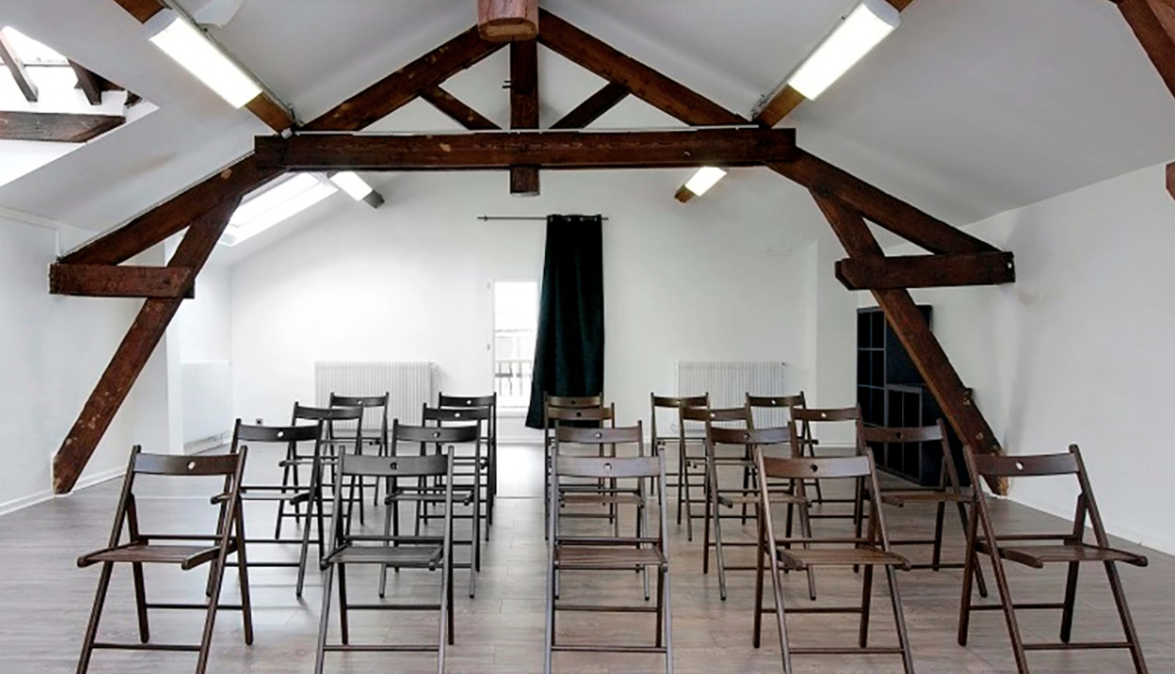 A spacious room with wooden beams overhead and rows of folding chairs arranged on a hardwood floor.